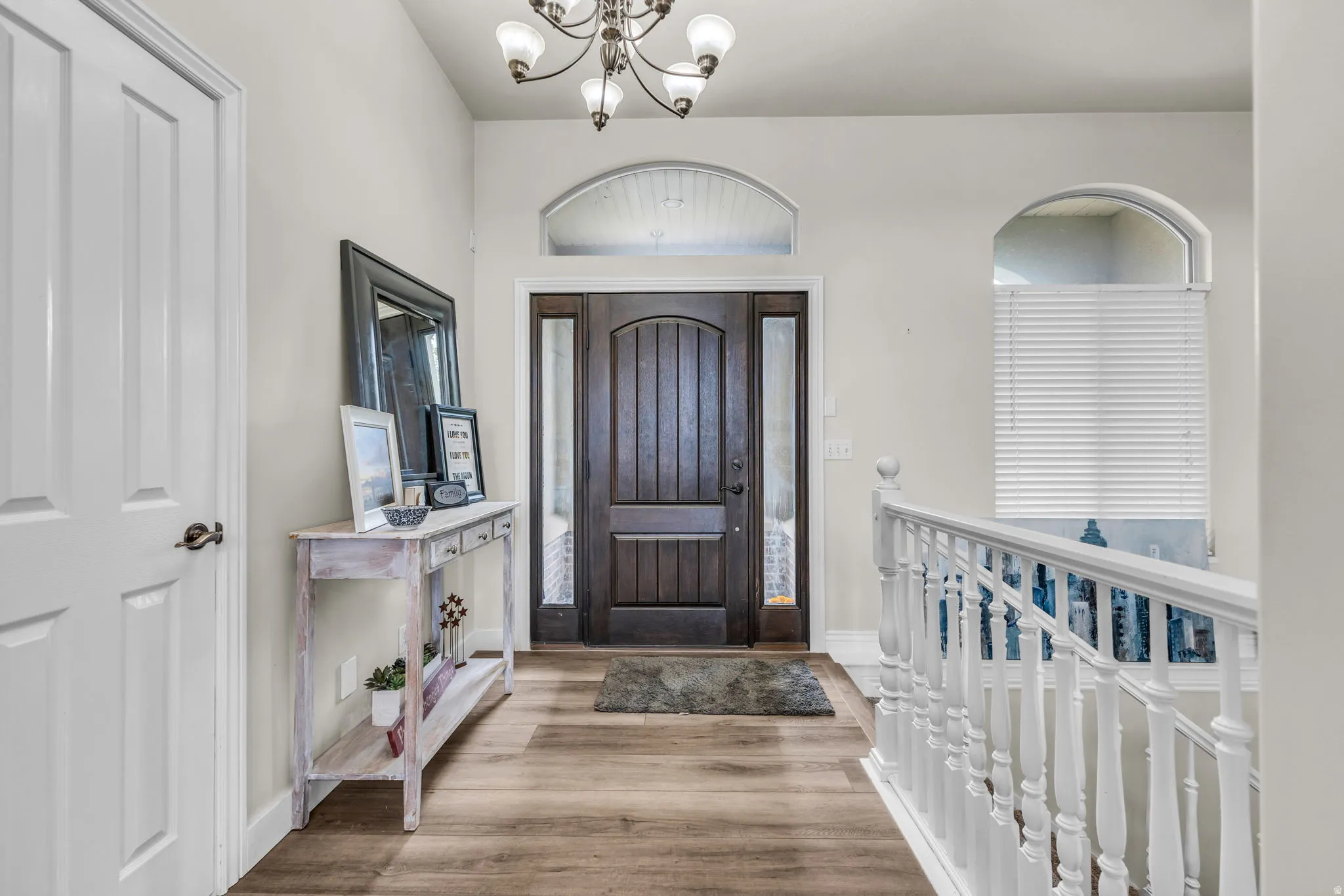 Entryway featuring a dark wood-finish door with sidelights, an arched transom window, wood-finish flooring, and a white baluster staircase