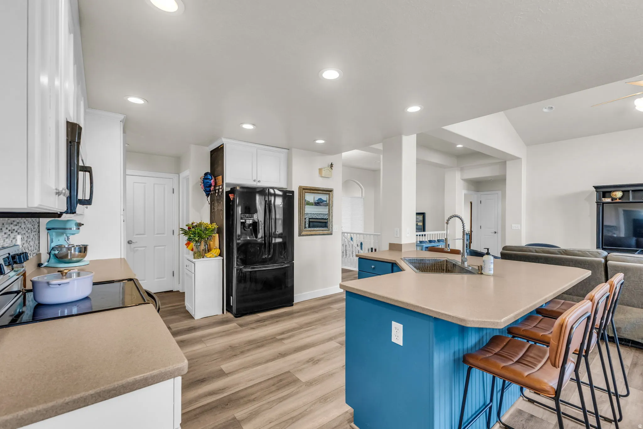 Open-concept kitchen with recessed lighting, light wood-finish flooring, and a central island featuring a stainless steel sink and breakfast bar seating