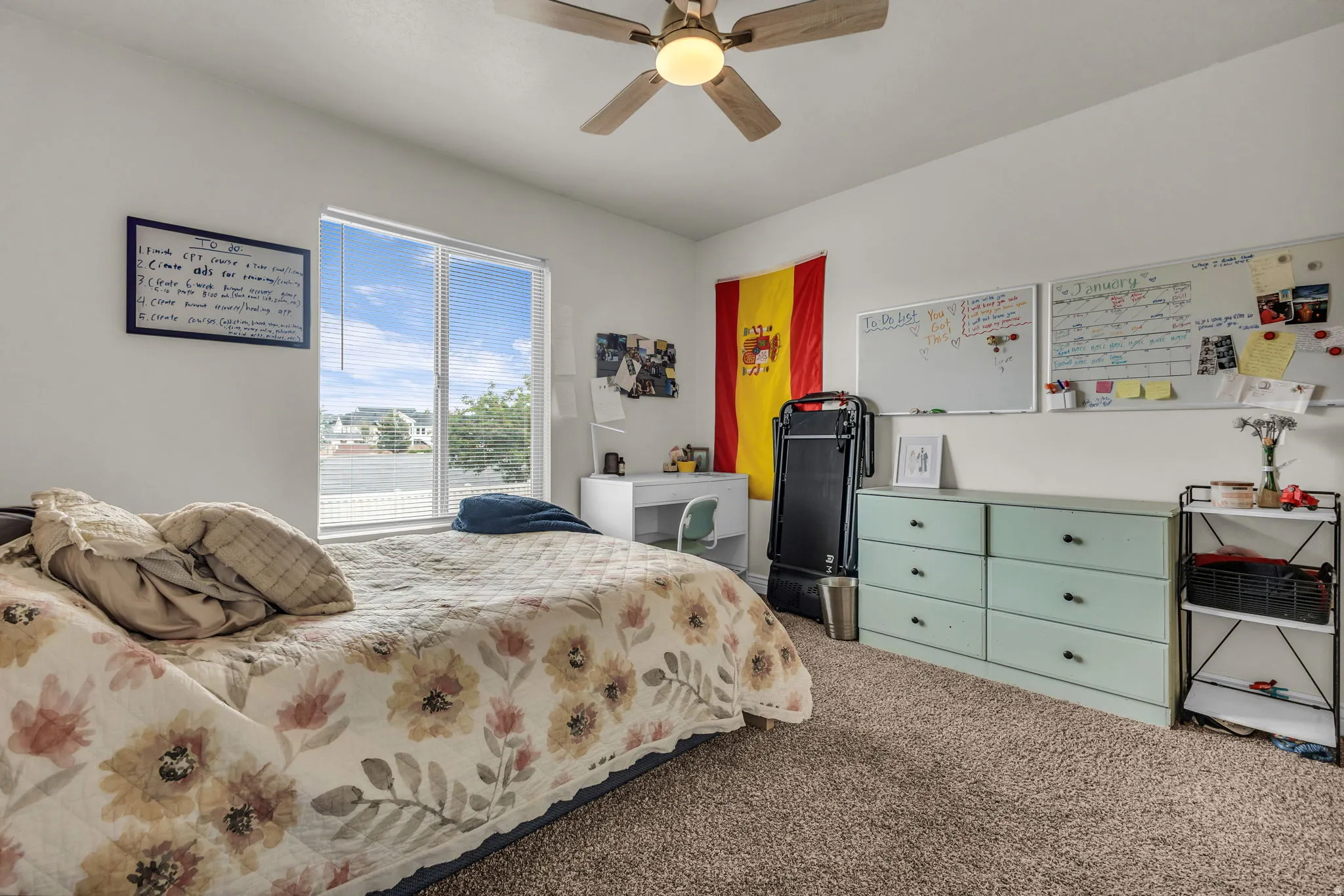 Spacious room featuring a ceiling fan with integrated lighting, a large window providing ample natural light, neutral wall paint, and plush carpeting