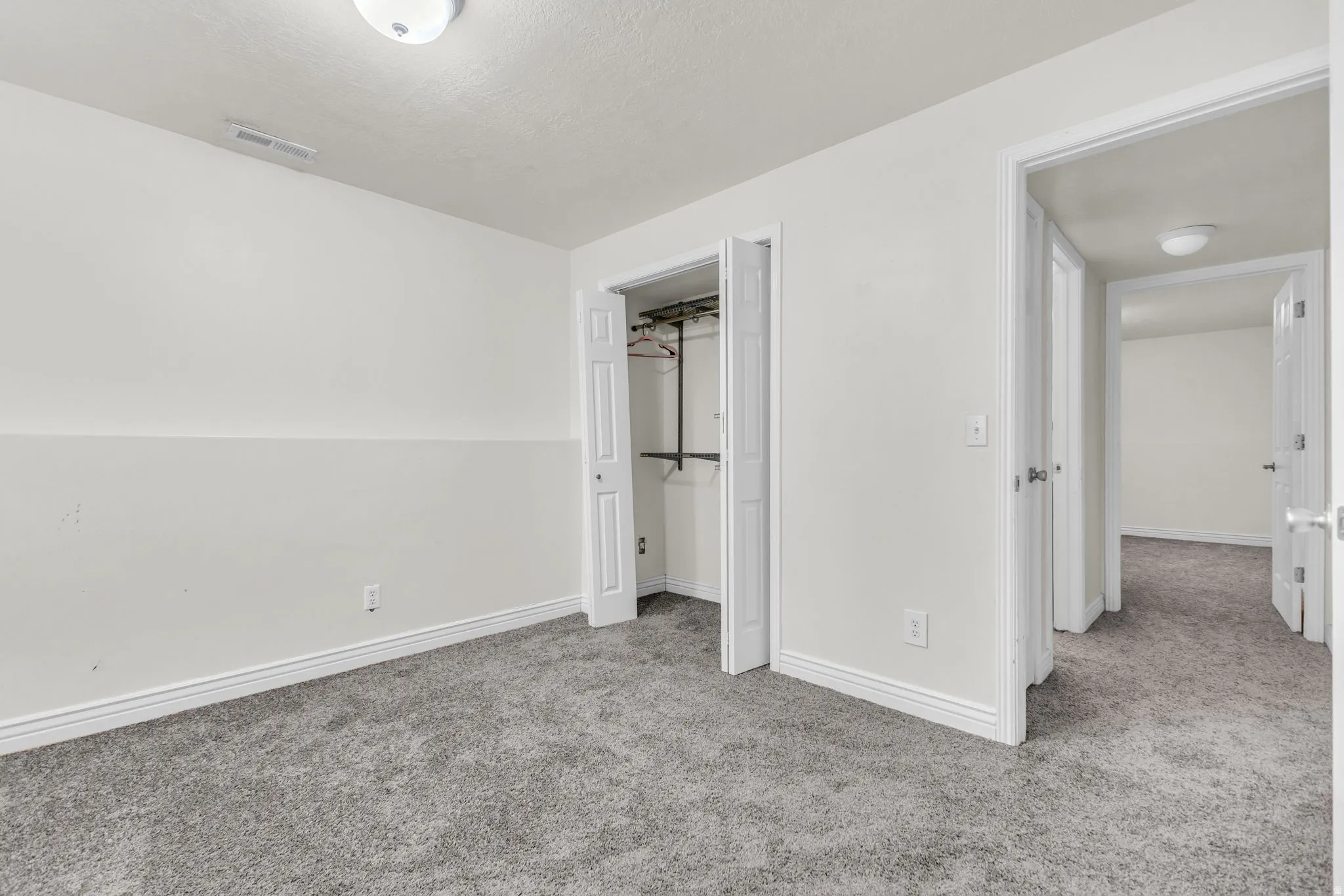 Neutral-toned room featuring grey textured carpeting and white baseboards