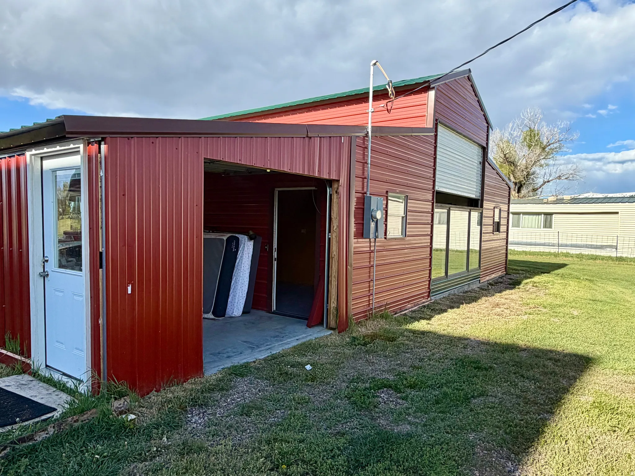 Red corrugated metal structure featuring a partial garage opening, a single white entry door, and multiple windows