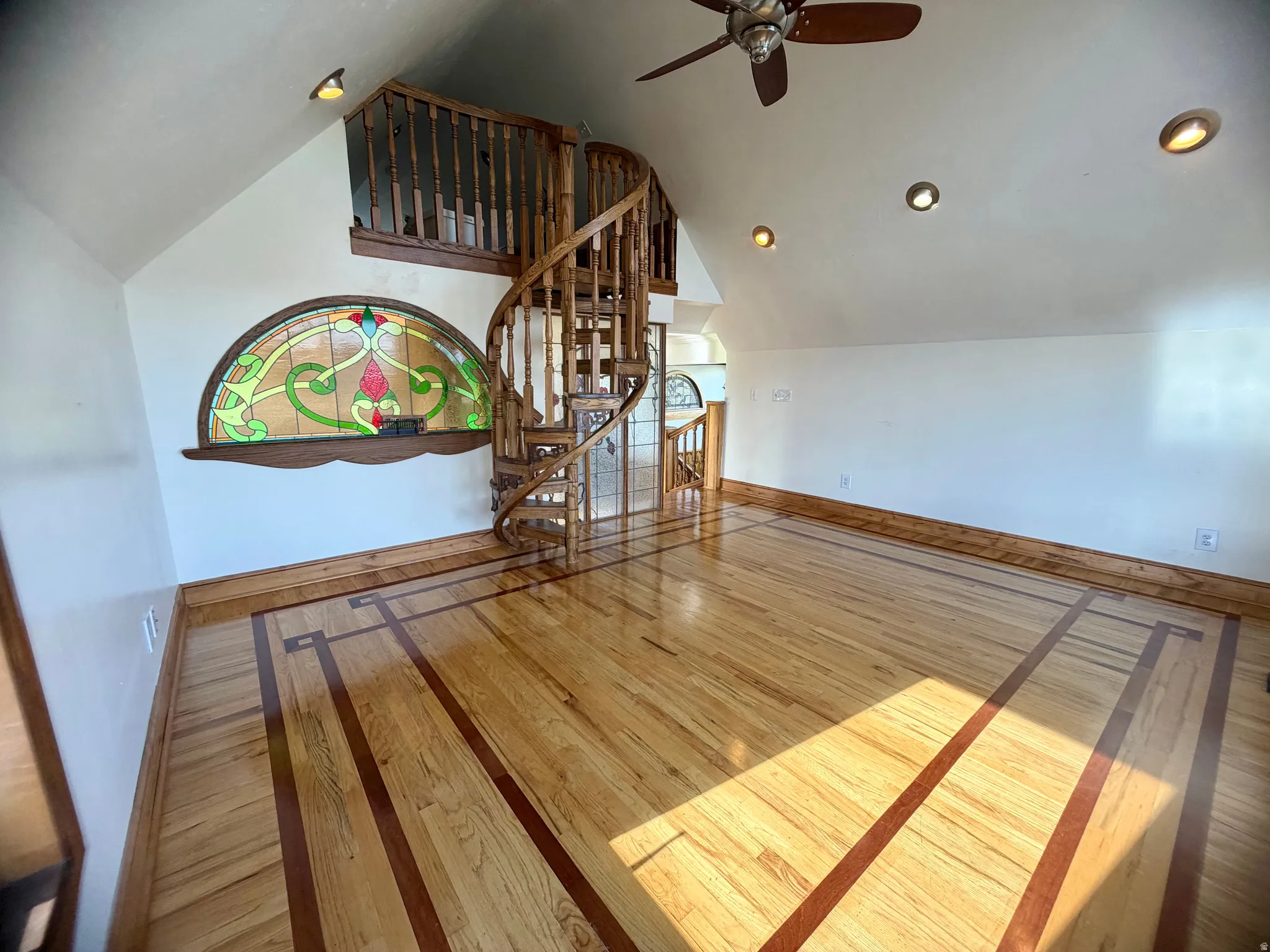 Wood-finish flooring with inlaid detailing, spiral staircase, and a stained-glass arched window feature