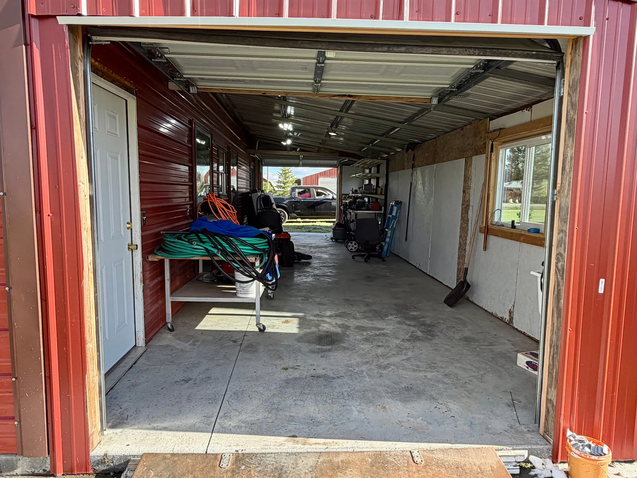 Red corrugated metal exterior with a large open bay, concrete flooring, interior access door, and an interior window