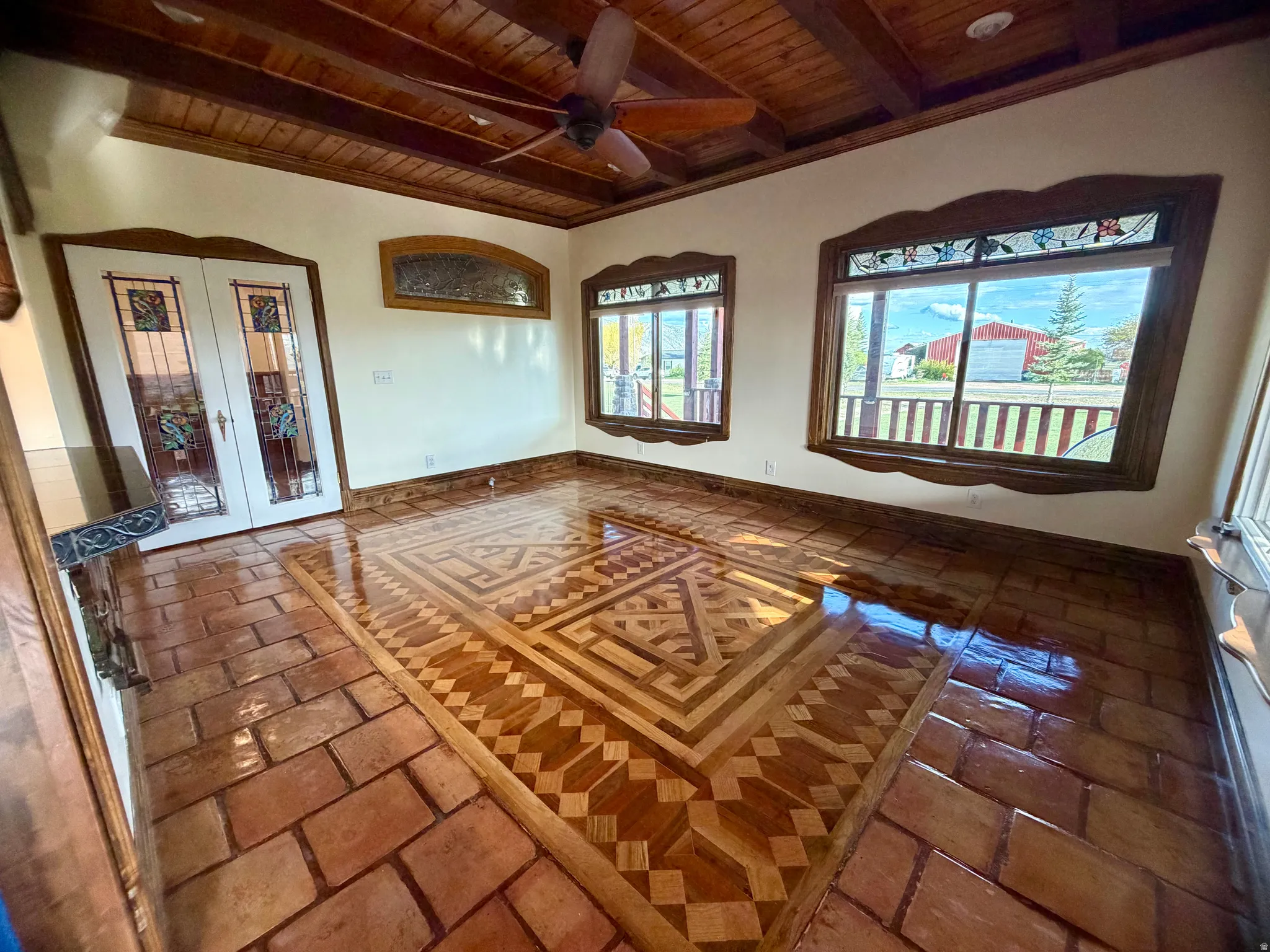 Exposed wood beam ceiling with a ceiling fan, decorative wood window frames with stained-glass accents, and a distinctive wood parquet floor inlay surrounded by tile flooring
