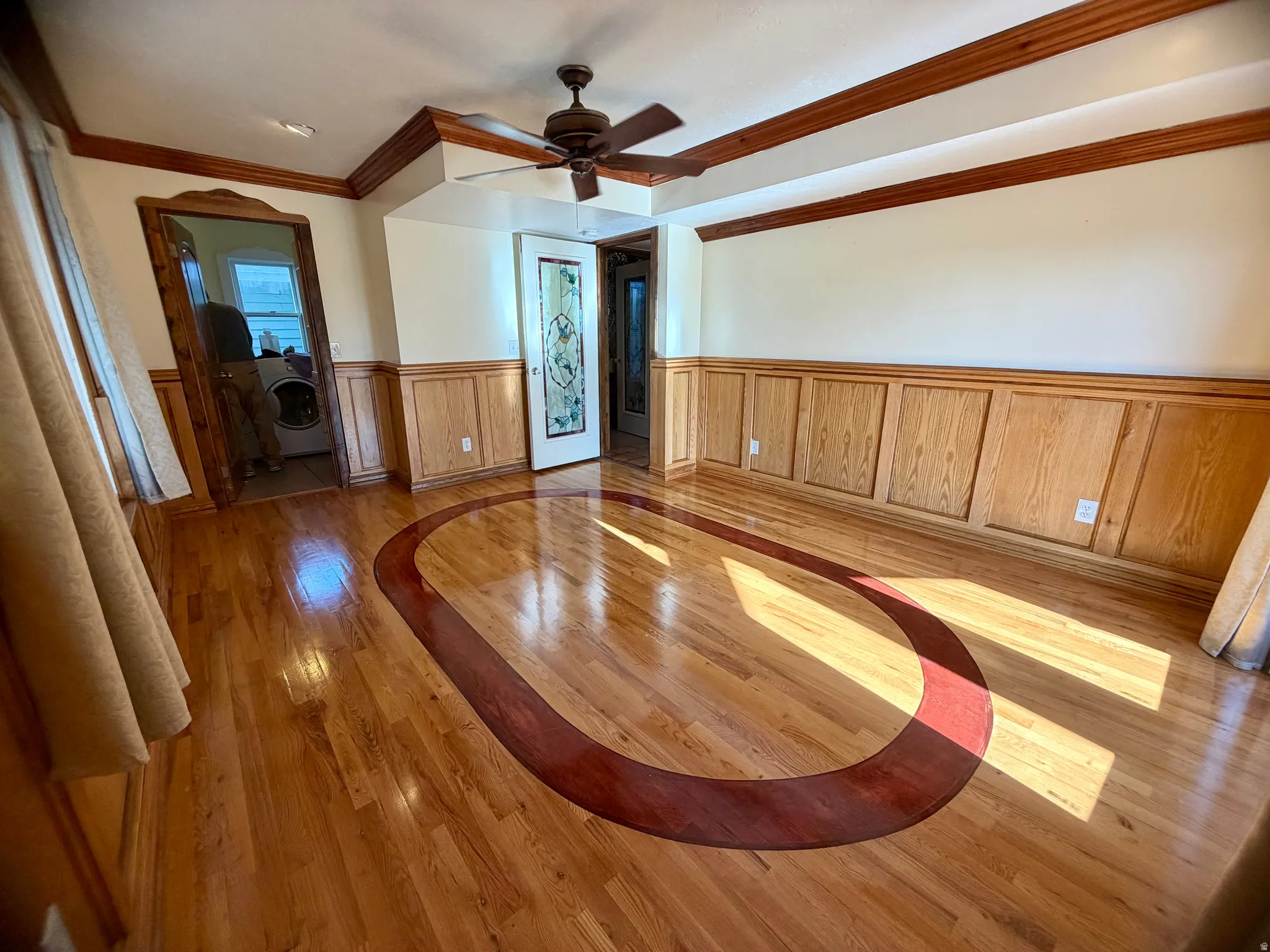 Expansive room featuring glossy wood-finish flooring with a contrasting inlay, wood paneling, and an ornate ceiling fan