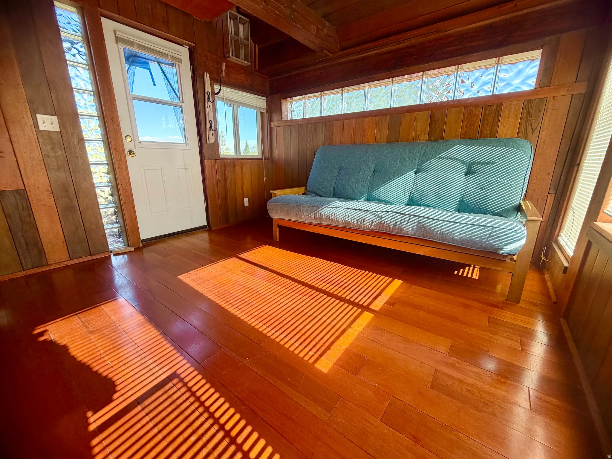 Room featuring wood-finish flooring, wood-paneled walls, multiple windows with blinds, and glass block window accents