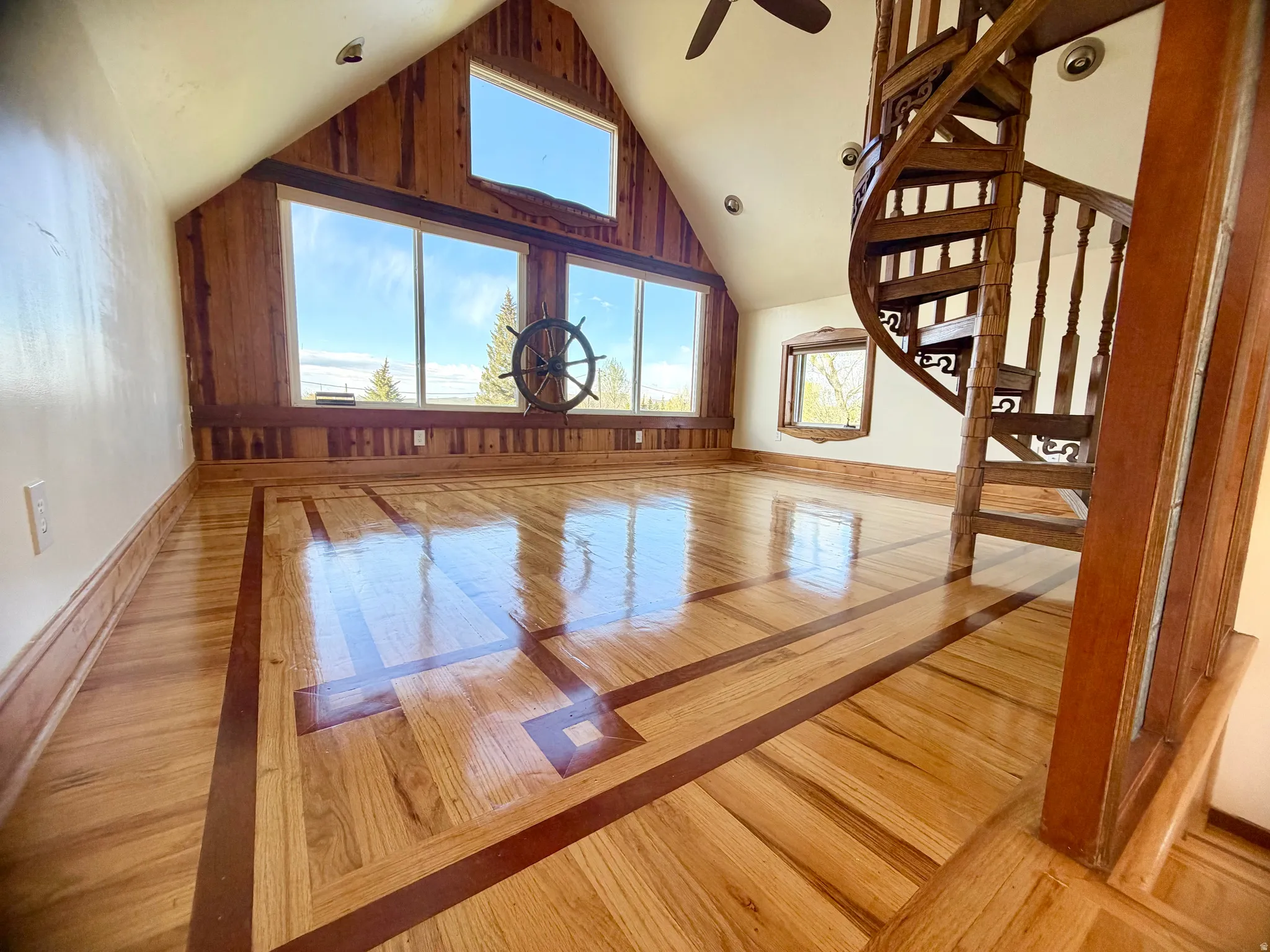 Attic room featuring a custom wooden spiral staircase, architectural windows, wood-finish flooring with intricate inlay, and wood-paneled walls