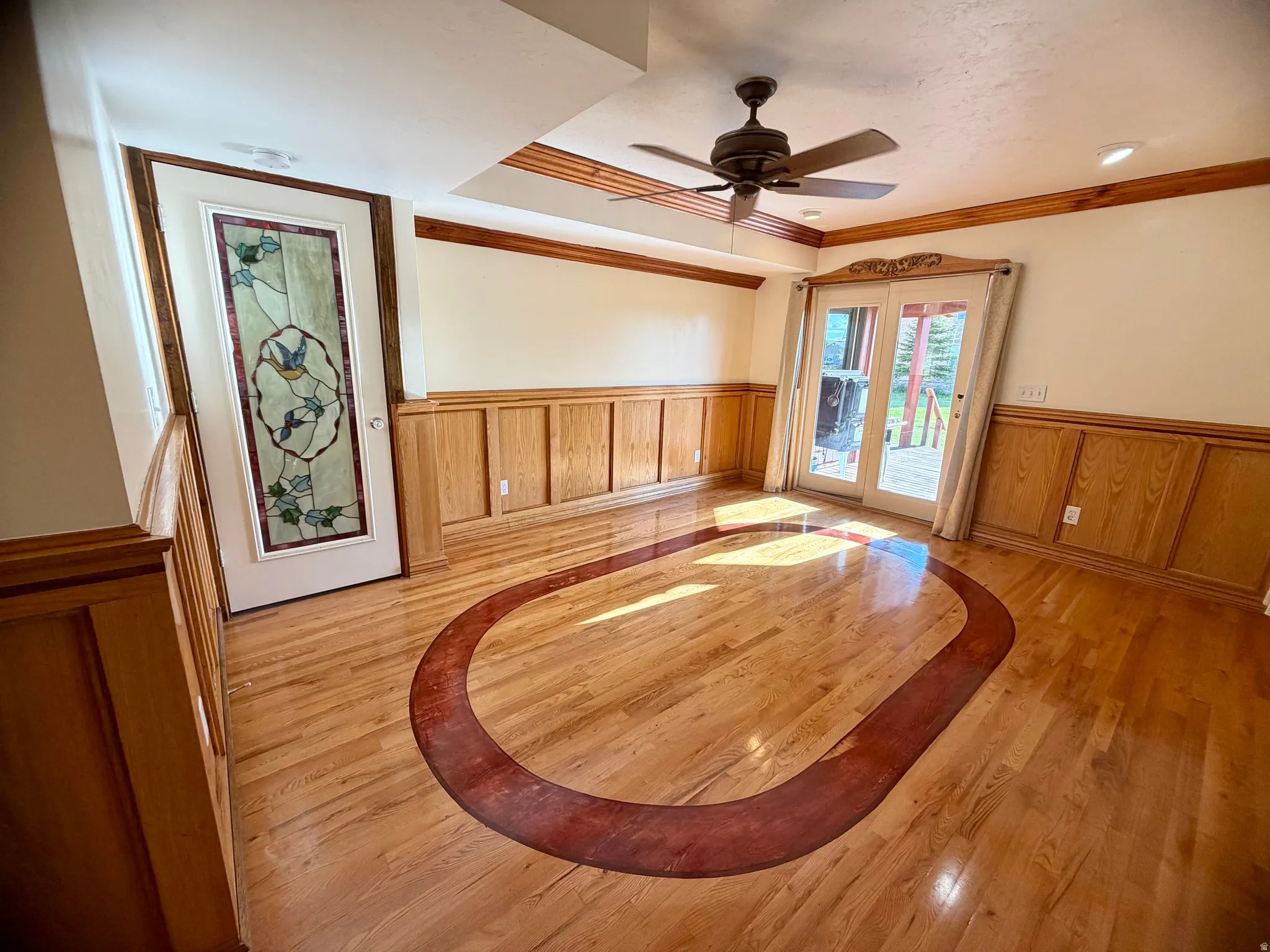 Hardwood flooring with a contrasting inlay, white wainscoting, and decorative wood trim