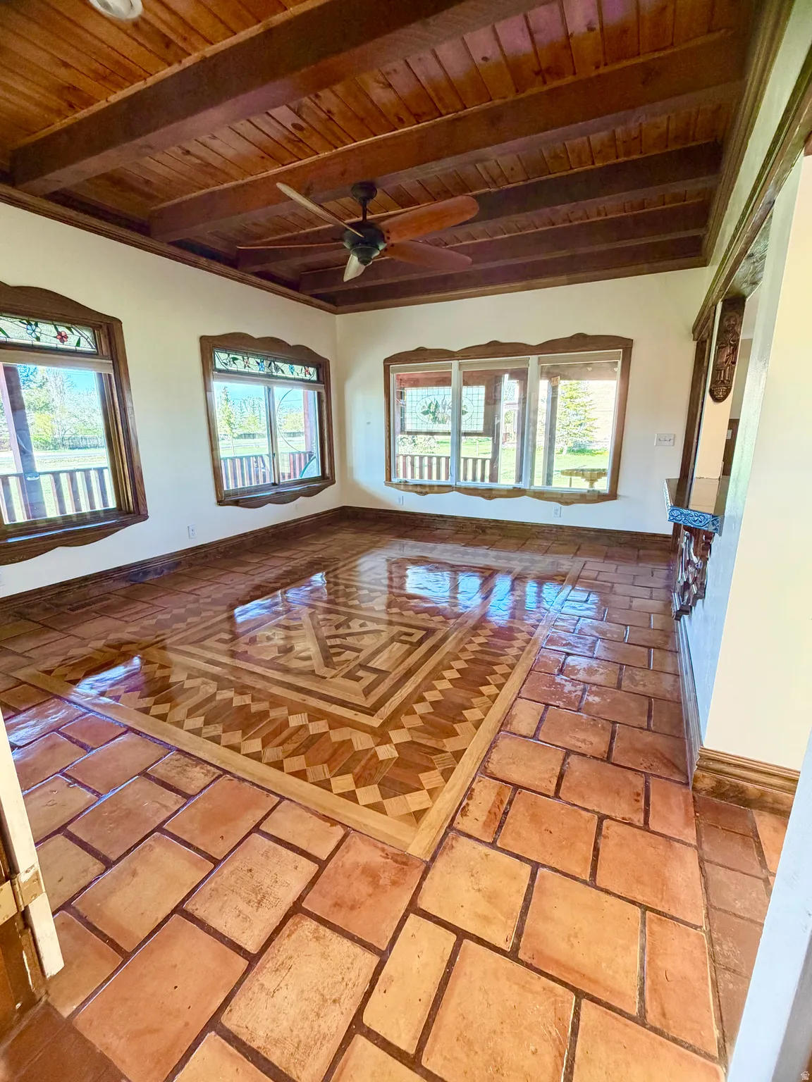 Room featuring a wood-panel ceiling with exposed beams, an integrated ceiling fan, and multiple windows