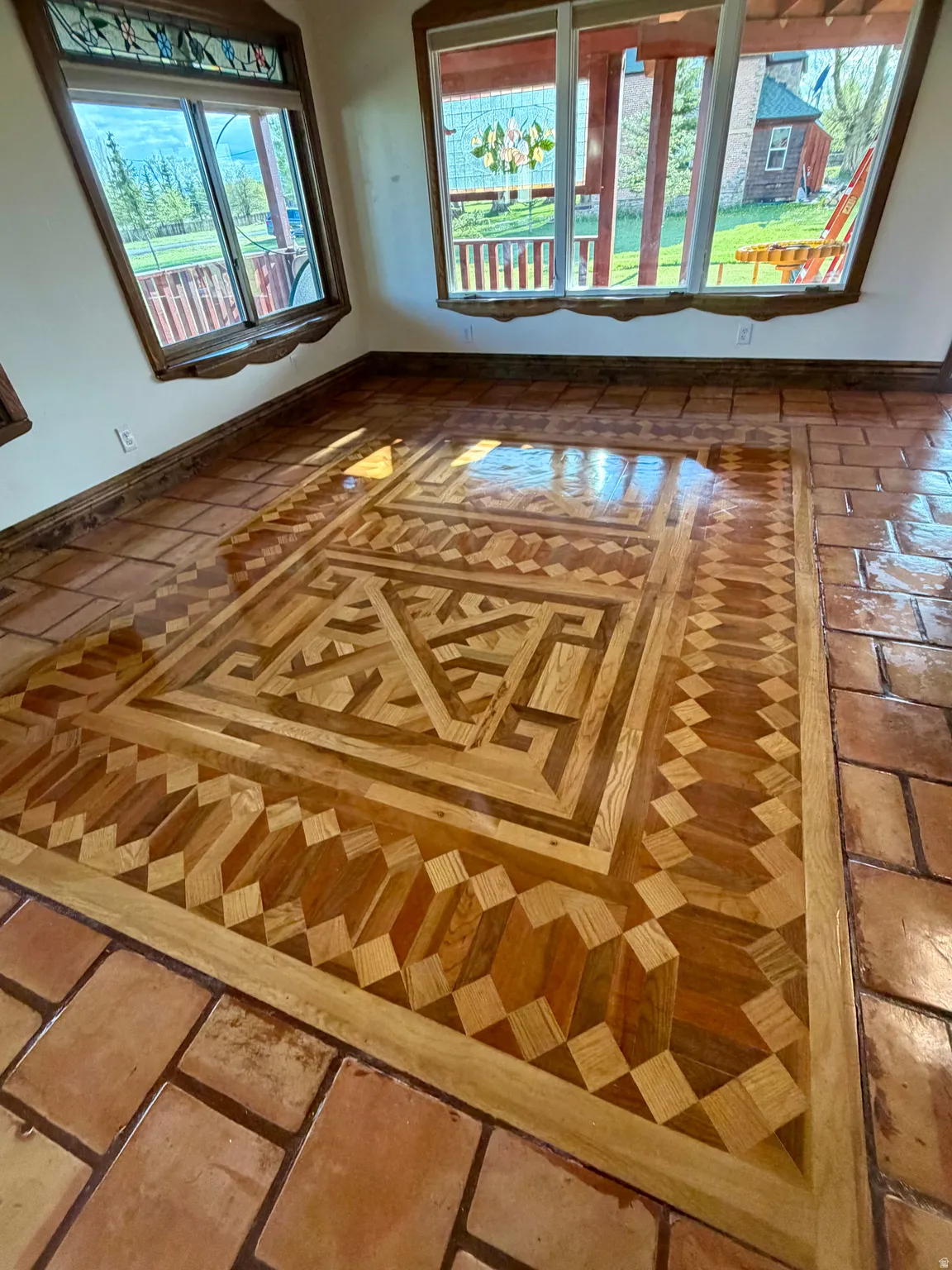 Hardwood marquetry flooring with a central geometric pattern, bordered by terracotta tile