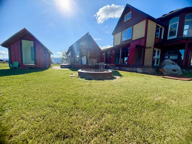 Expansive lawn area featuring a central fire pit, two separate outbuildings with red siding, and a main residence with a covered porch