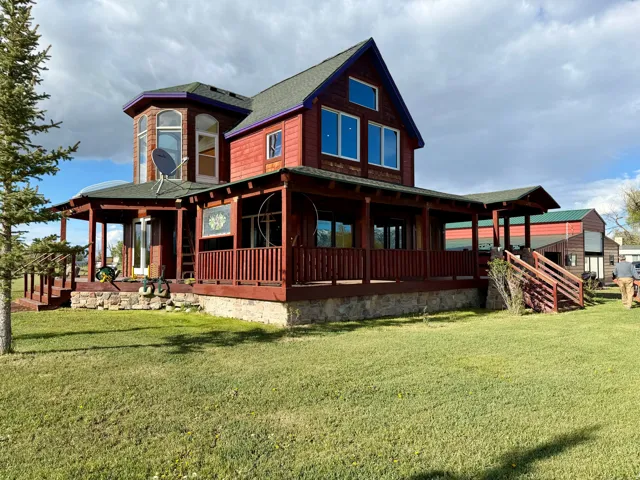 Red-sided residence featuring a stone foundation and a wrap-around covered porch