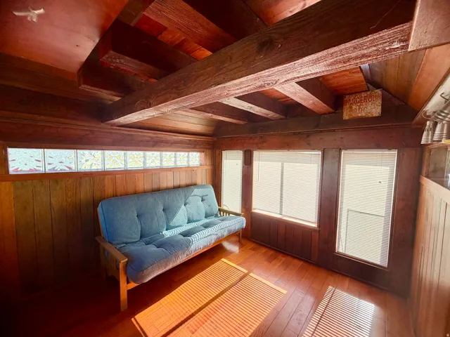 Wood-paneled room featuring exposed ceiling beams and wood-finish flooring