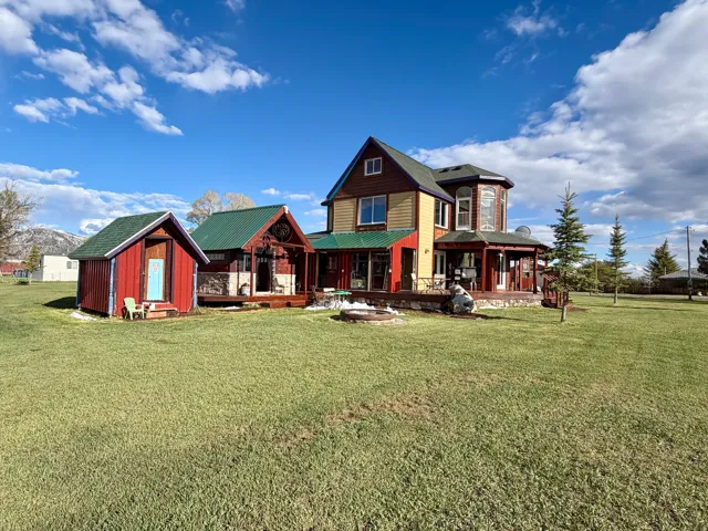 Expansive green lawn bordering a multi-level residence featuring a wrap-around porch and a detached outbuilding