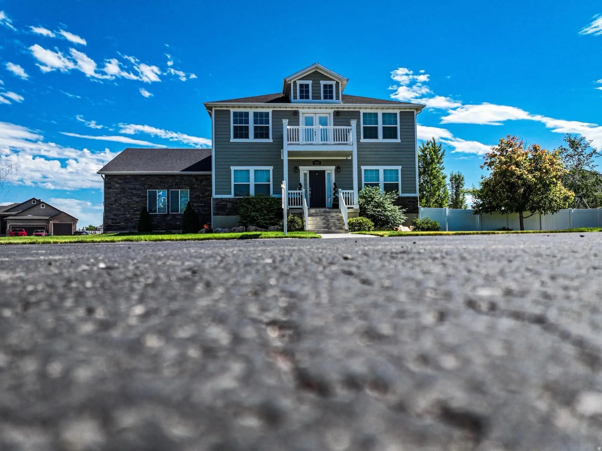 Two-story residence featuring a central balcony, multiple dormer windows, and a combination of siding and stone veneer