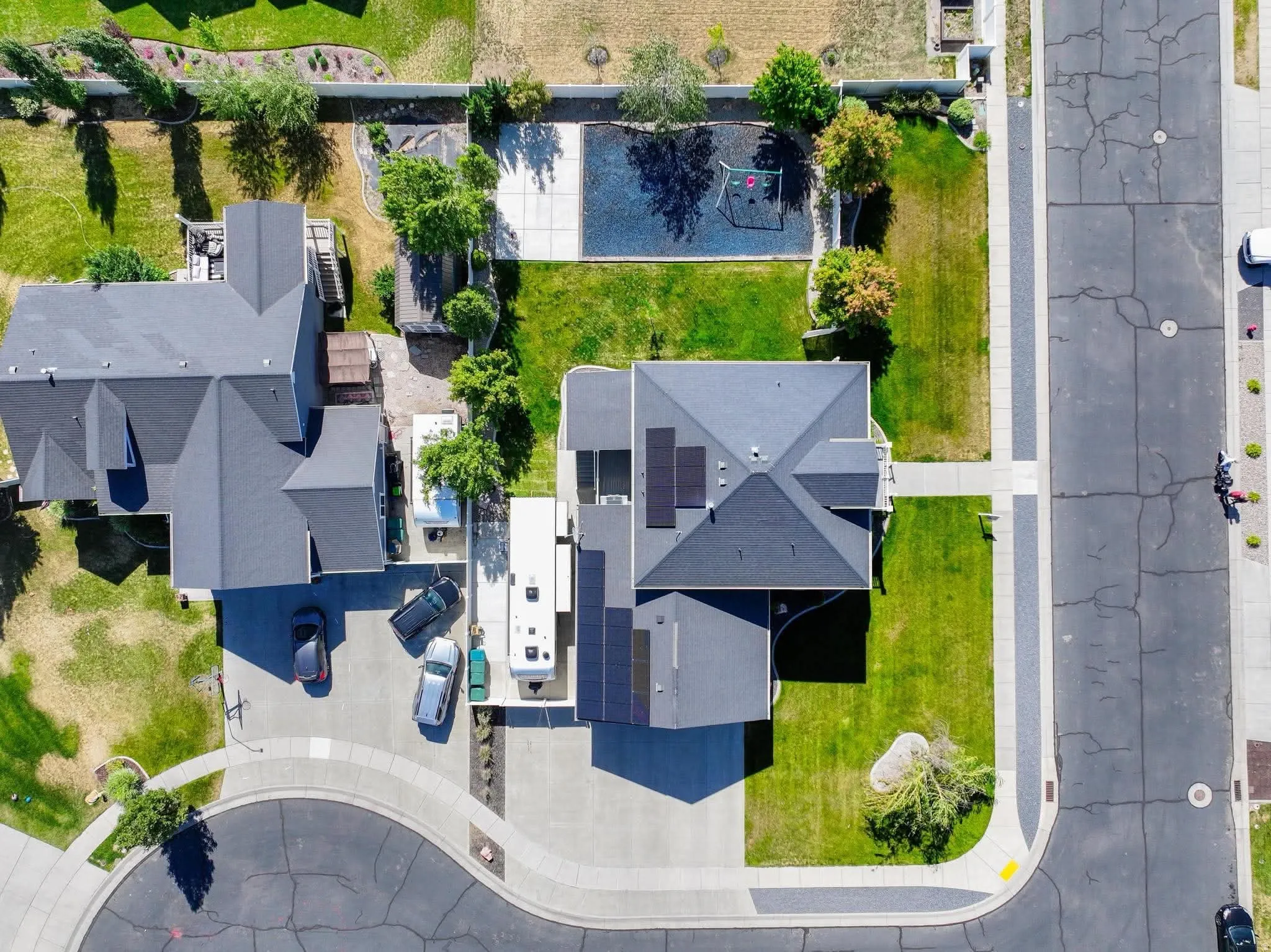 Property featuring a dark shingle roof with integrated solar panels, a paved driveway, and a front yard with manicured lawn