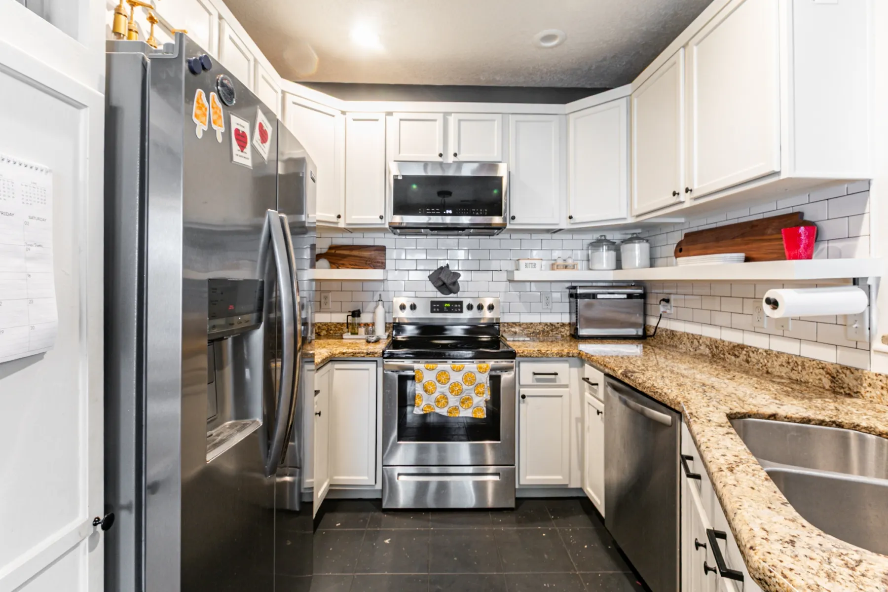 Modern kitchen featuring white cabinetry with black hardware, stainless steel appliances, granite countertops, and a white subway tile backsplash