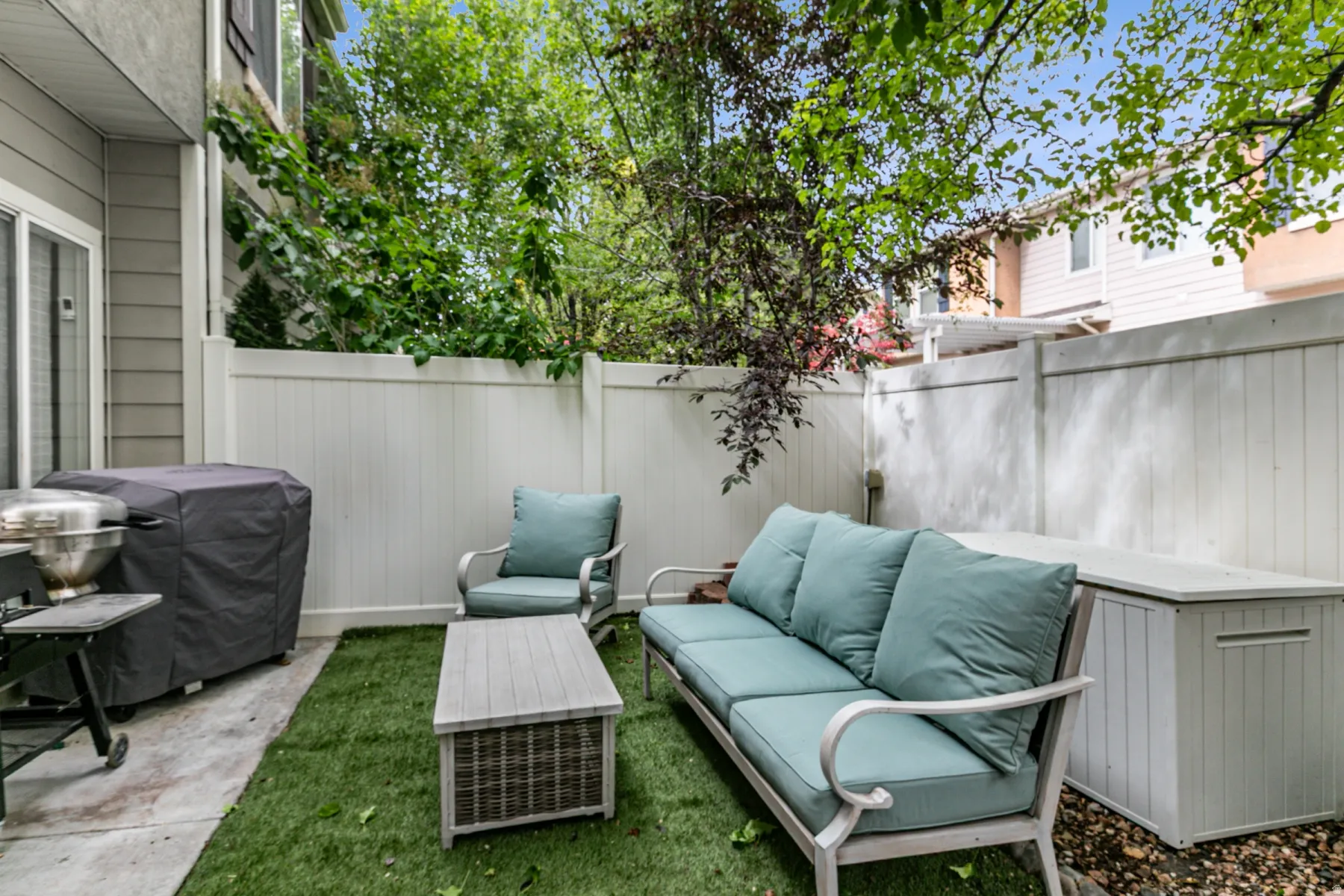 Private patio space featuring artificial turf, a concrete pad, and white privacy fencing