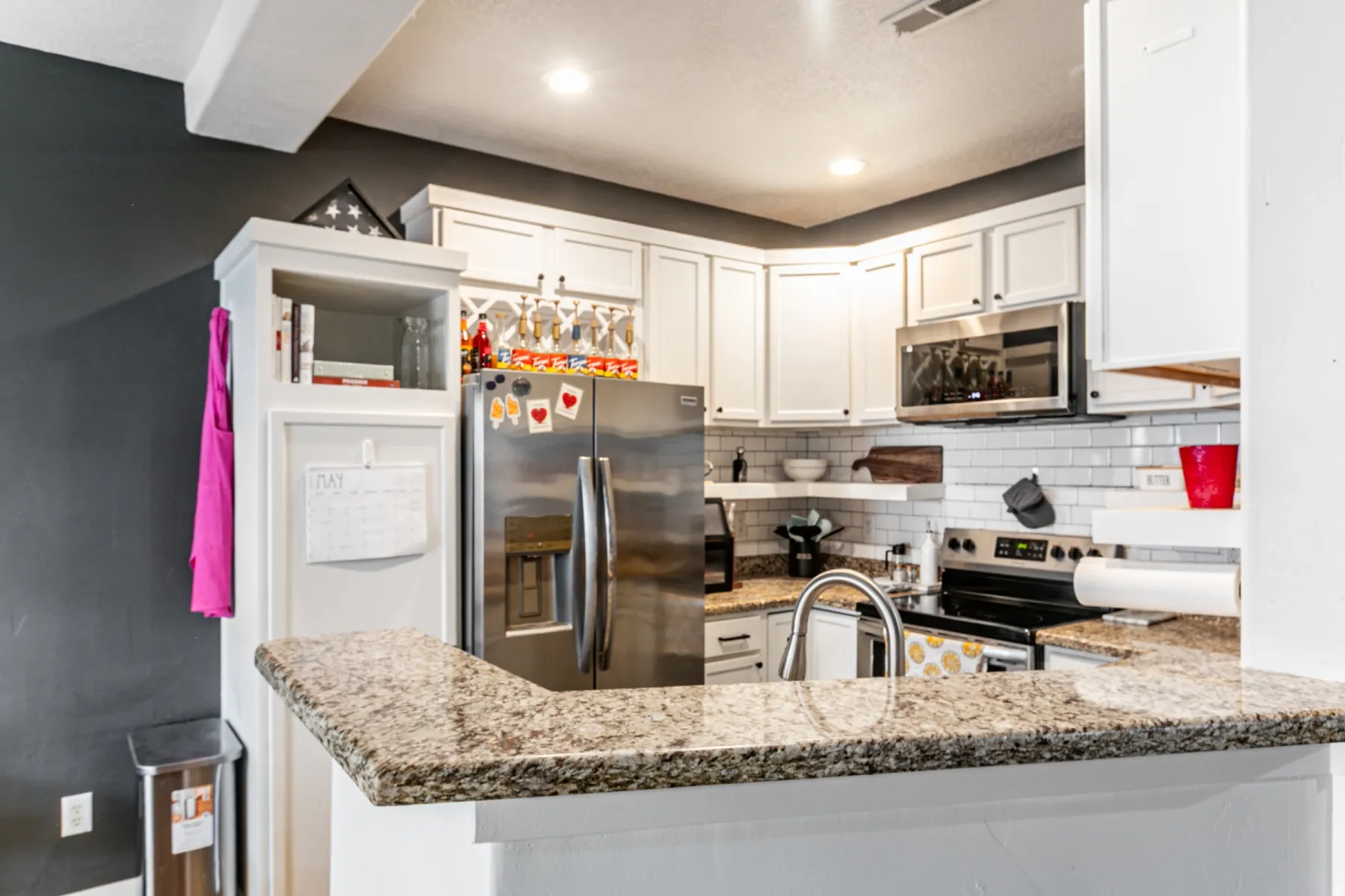 Kitchen featuring white cabinetry, stainless steel appliances, speckled stone countertops, and a white subway tile backsplash