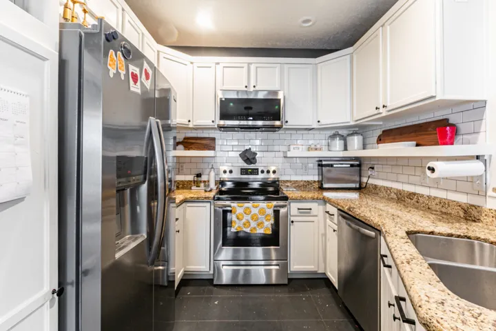 Modern kitchen featuring white cabinetry with black hardware, stainless steel appliances, granite countertops, and a white subway tile backsplash