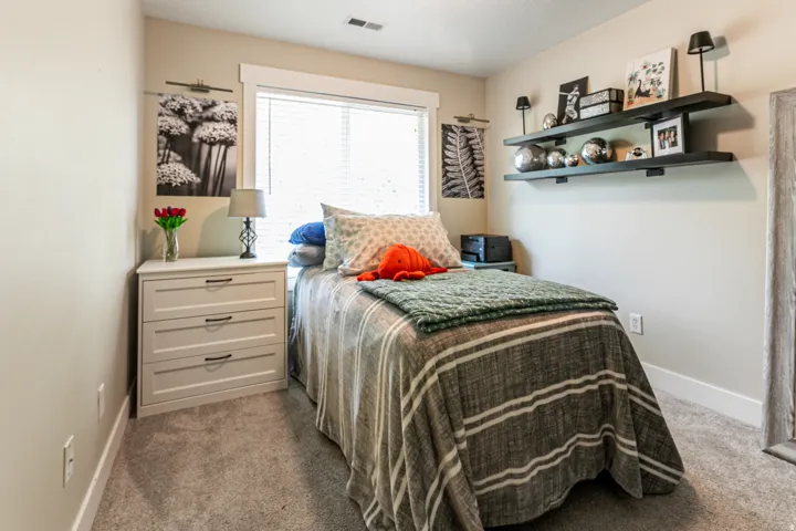 Carpeted bedroom two featuring a single window with blinds, white trim, and light beige walls