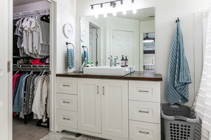 Primary bathroom vanity featuring a vessel sink, dark wood-finish countertop, white cabinetry with bronze hardware, and a large mirror with track lighting
