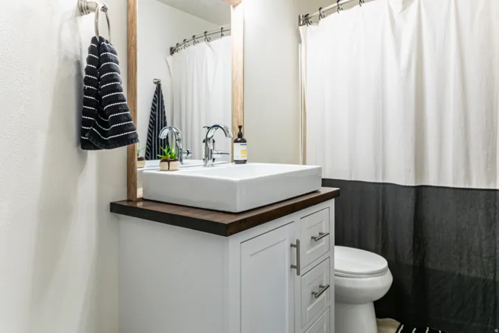 Bathroom featuring a vessel sink atop a dark wood-finish countertop, white cabinetry with silver-tone hardware, and a framed mirror