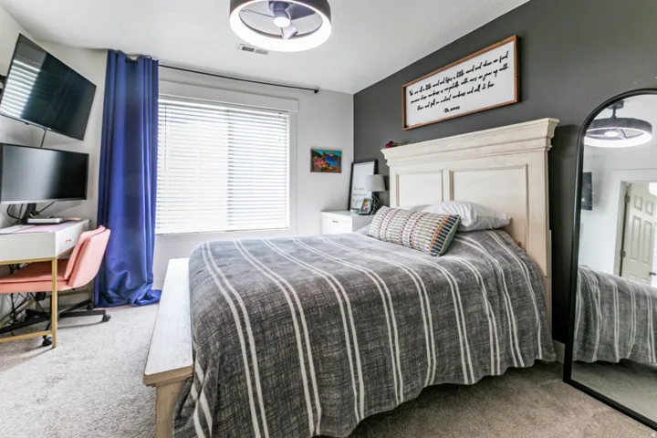 Primary bedroom featuring a paneled headboard, carpet flooring, a window with blinds, and a contemporary ceiling light fixture