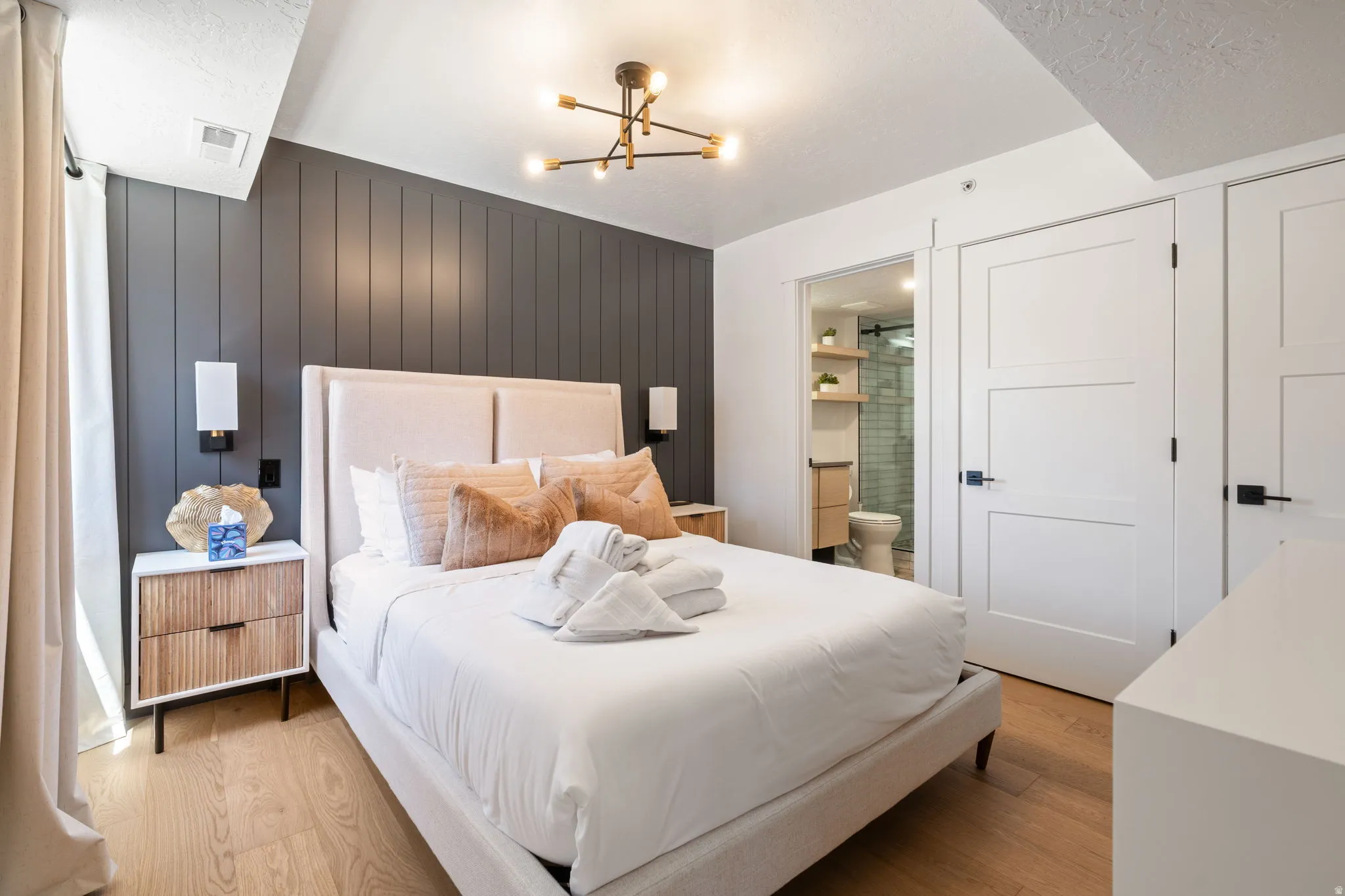 Bedroom featuring a paneled accent wall, wood-finish flooring, and a modern ceiling light fixture