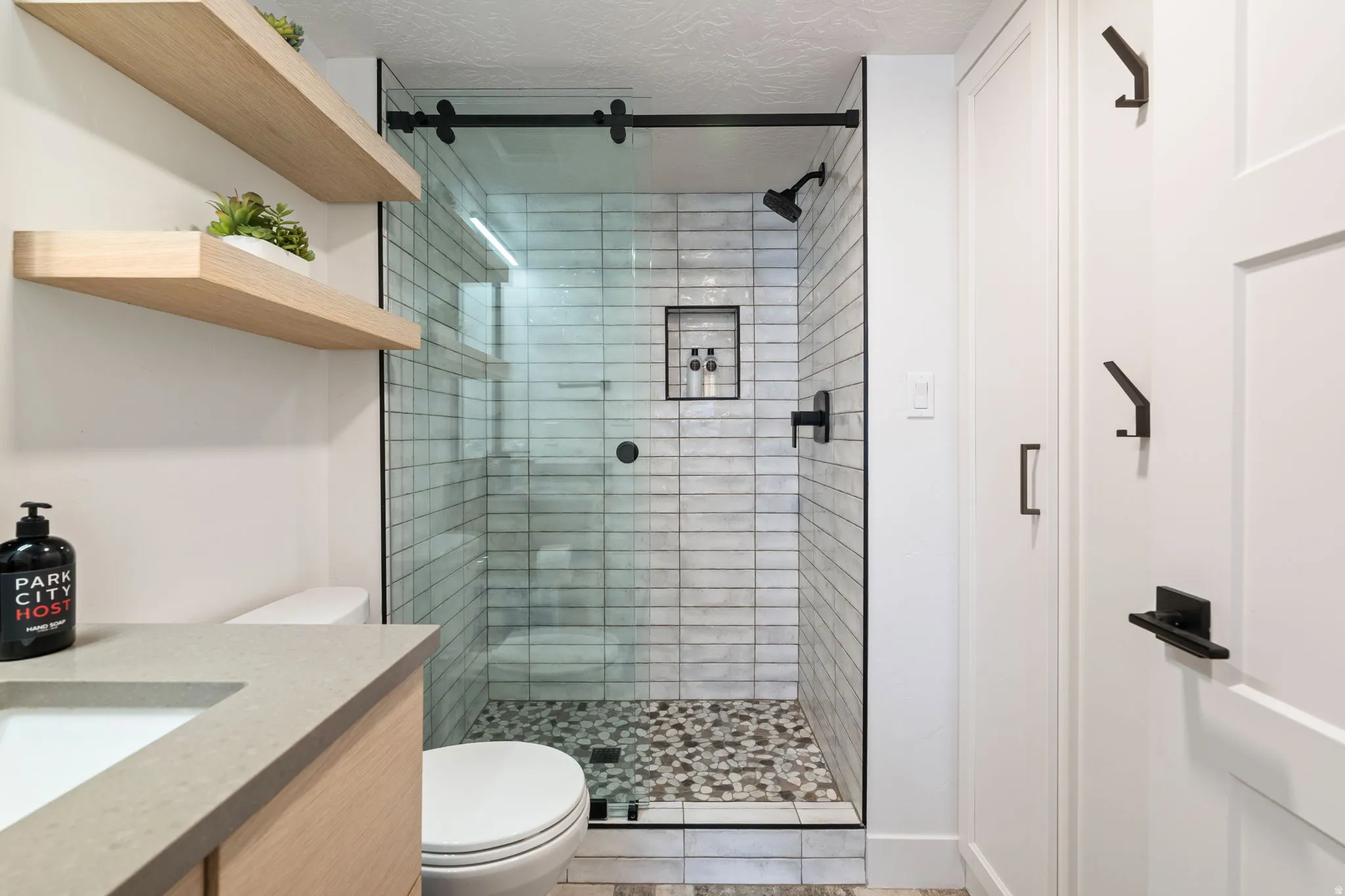 Glass-enclosed shower with subway tile surround and pebble-style flooring