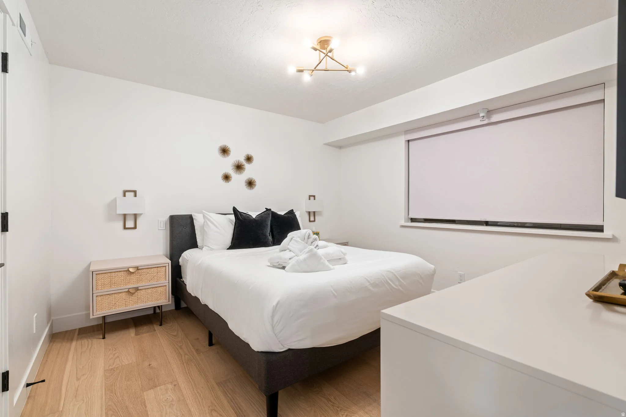 Bedroom featuring wood-finish flooring, white walls, and a recessed window with a roller shade