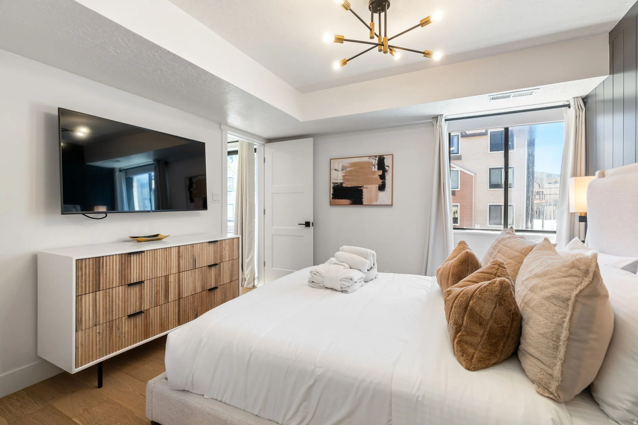 Spacious room featuring a large window, light wood-finish flooring, and a modern chandelier