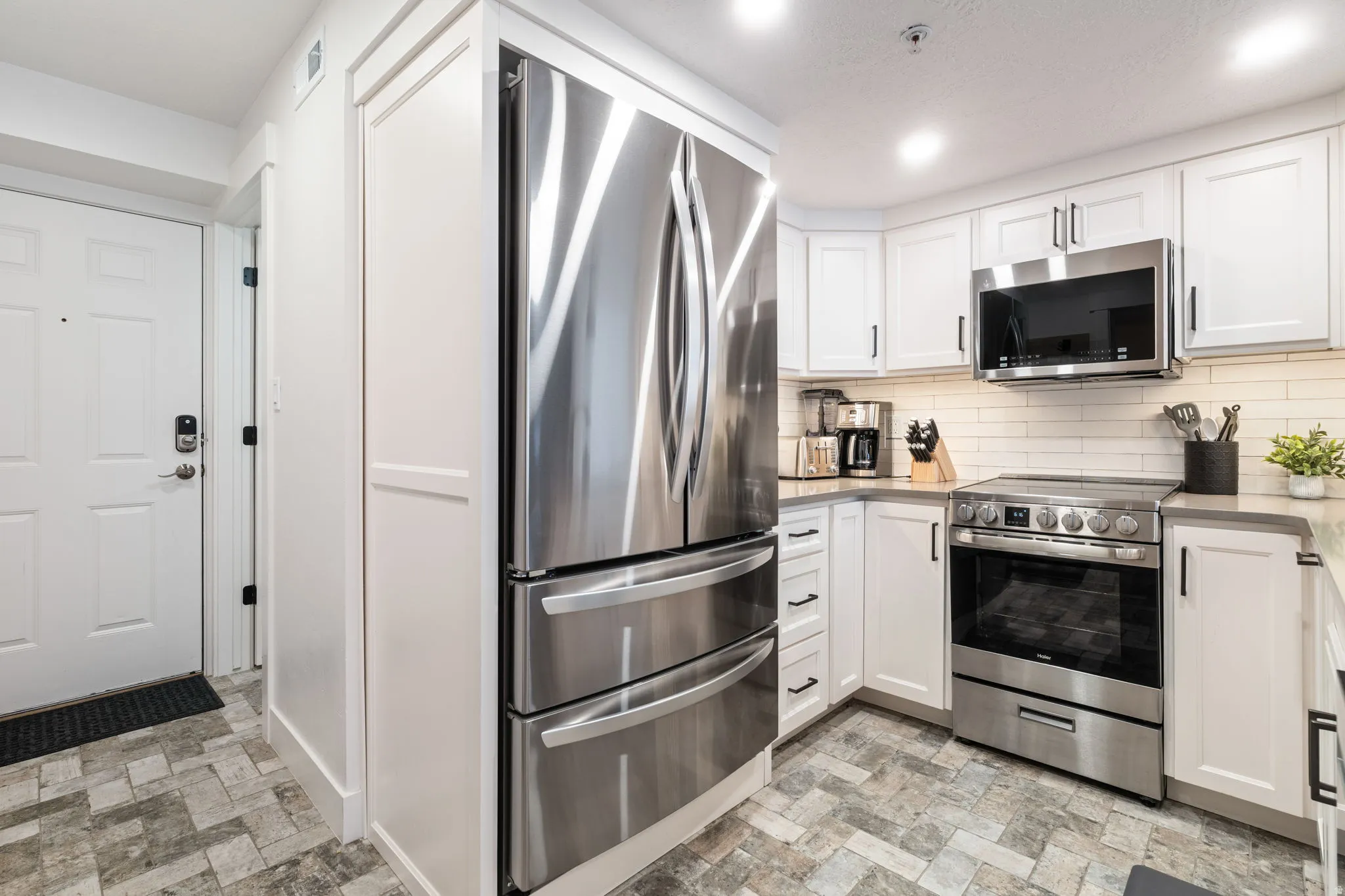 Contemporary kitchen featuring white cabinetry, subway tile backsplash, stainless steel appliances, and patterned flooring