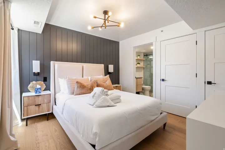 Bedroom featuring a paneled accent wall, wood-finish flooring, and a modern ceiling light fixture