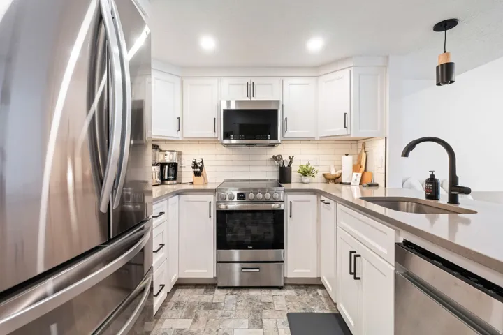 Kitchen featuring white cabinetry, stainless steel appliances, a subway tile backsplash, light-toned countertops, and mosaic-style flooring