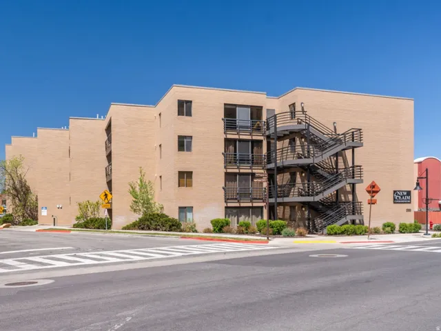 Multi-story brick building featuring balconies with metal railings, exterior metal stairwells, and mature landscaping