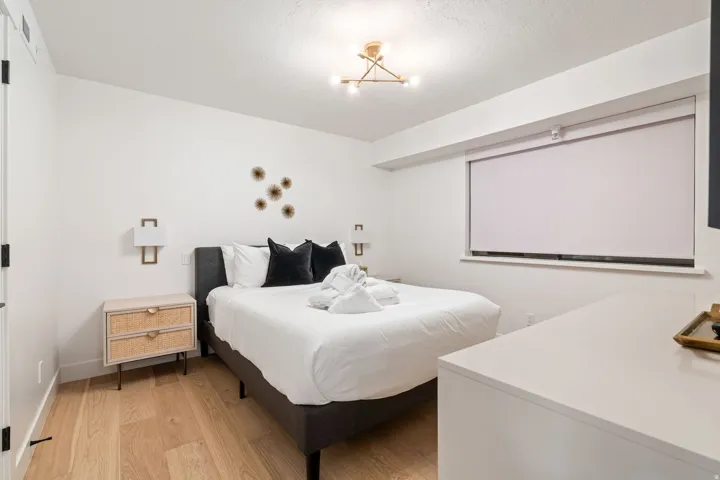 Bedroom featuring wood-finish flooring, white walls, and a recessed window with a roller shade