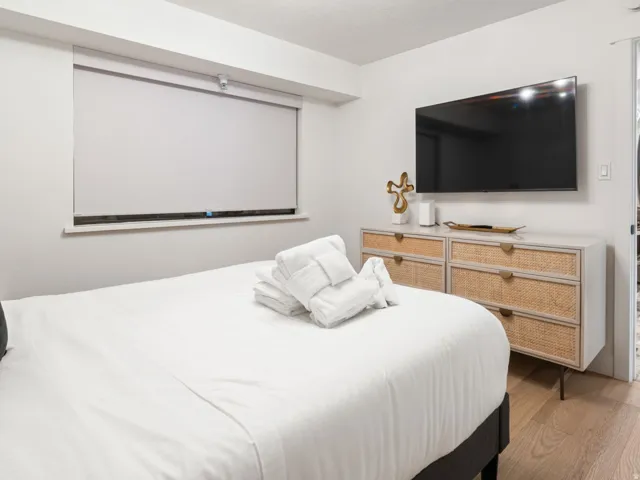 Bedroom featuring a window with a roller shade, wood-finish flooring, and a contemporary light fixture