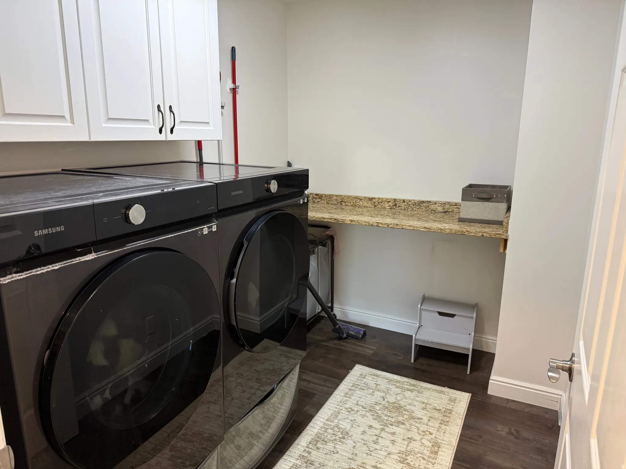 Laundry area featuring wood-finish flooring, white cabinetry with dark hardware, and a granite-look countertop