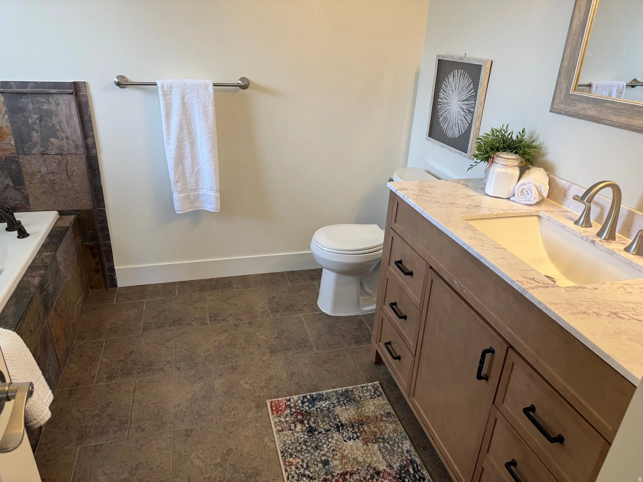 Spacious bathroom featuring a single vanity with stone-finish countertop, undermount sink, and brushed nickel faucet