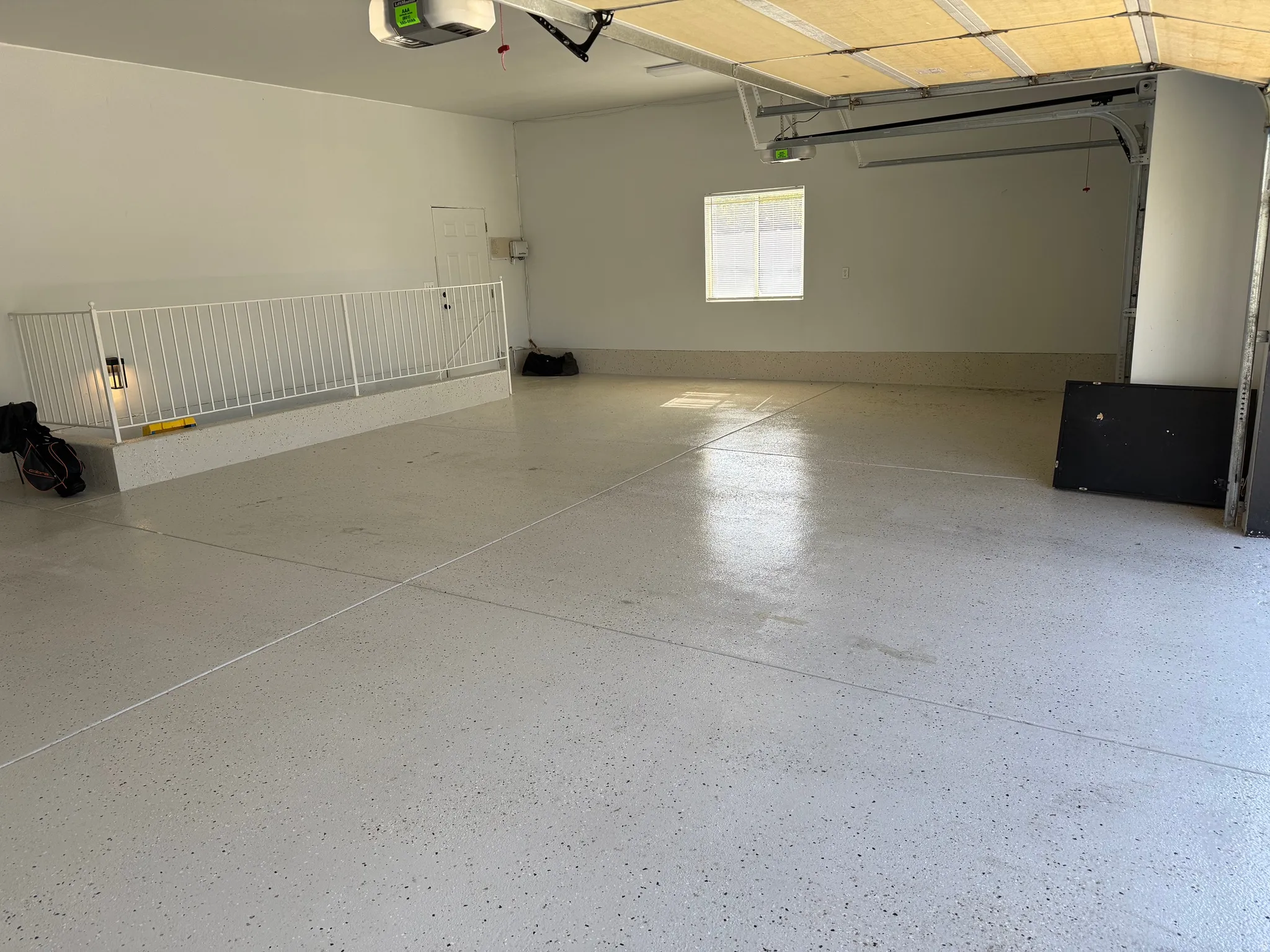 Spacious oversized 3 car garage featuring a light-toned epoxy floor, integrated overhead door mechanisms, and a built-in elevated storage platform with railing