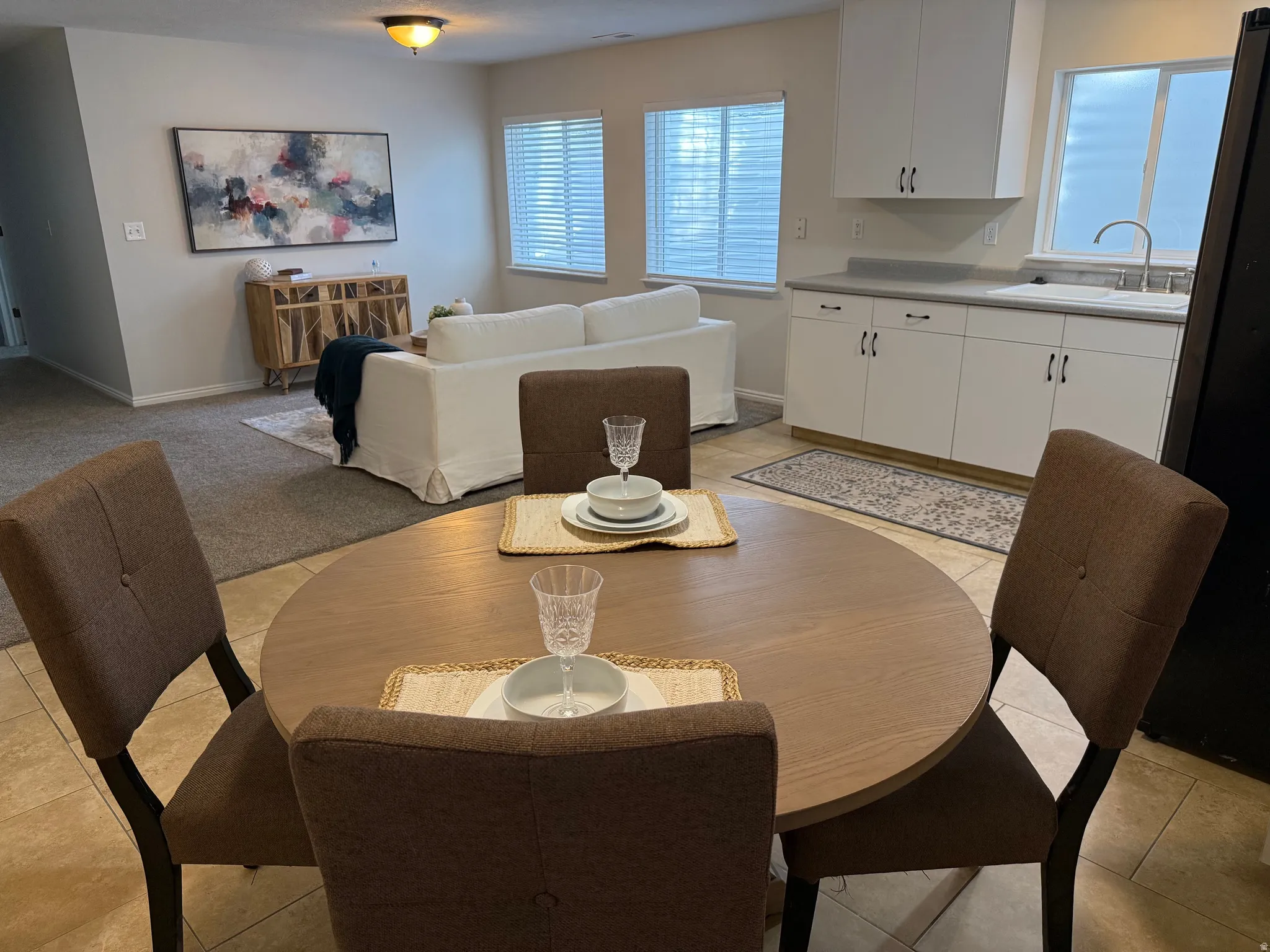 Open-concept living space featuring a kitchen with white cabinetry and a stainless steel sink, tile flooring, and two windows with blinds