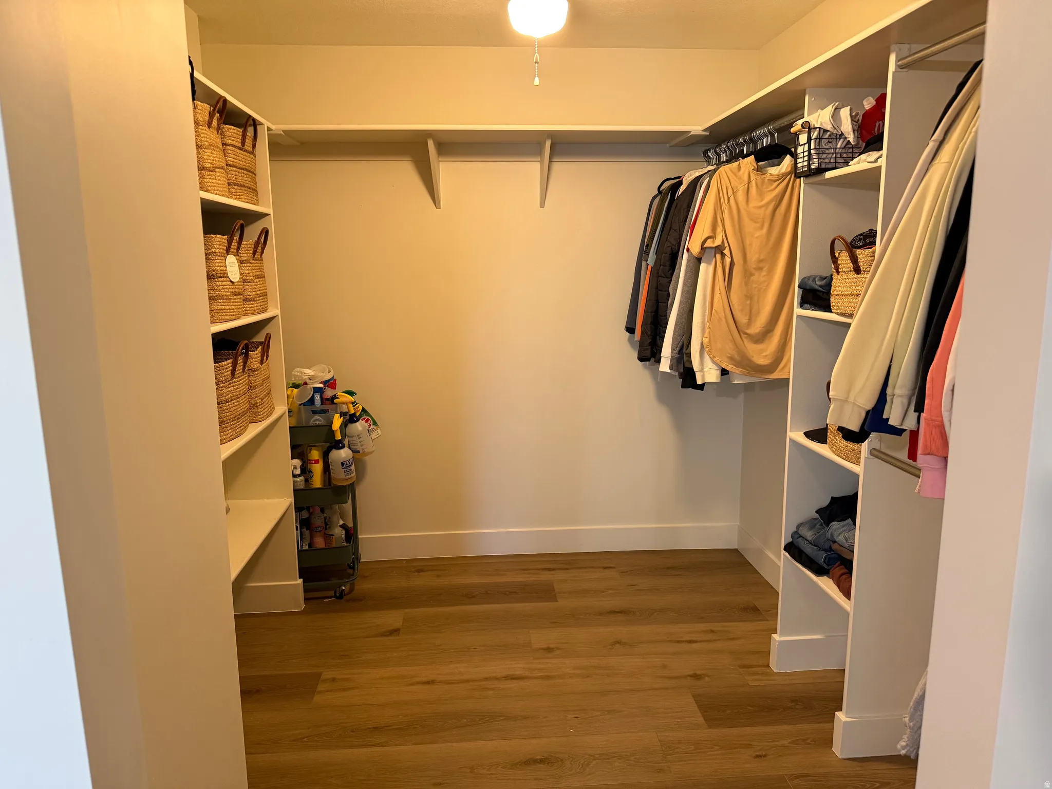 Expansive master closet featuring wood-finish flooring, white baseboards, built-in shelving, and multiple clothing rods