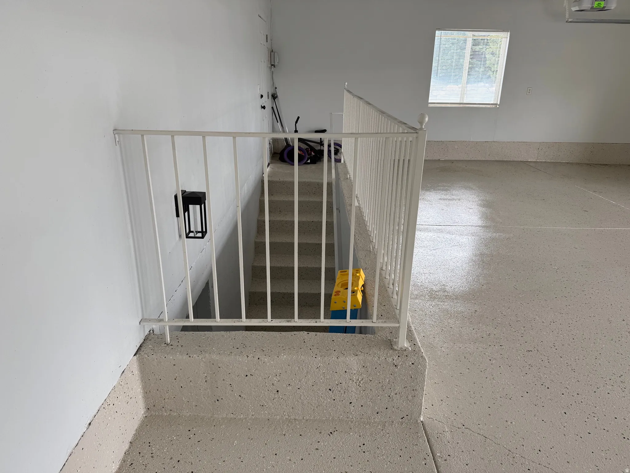 Wide Stairwell entry to basement featuring a white metal railing, painted walls, and a wall-mounted light fixture