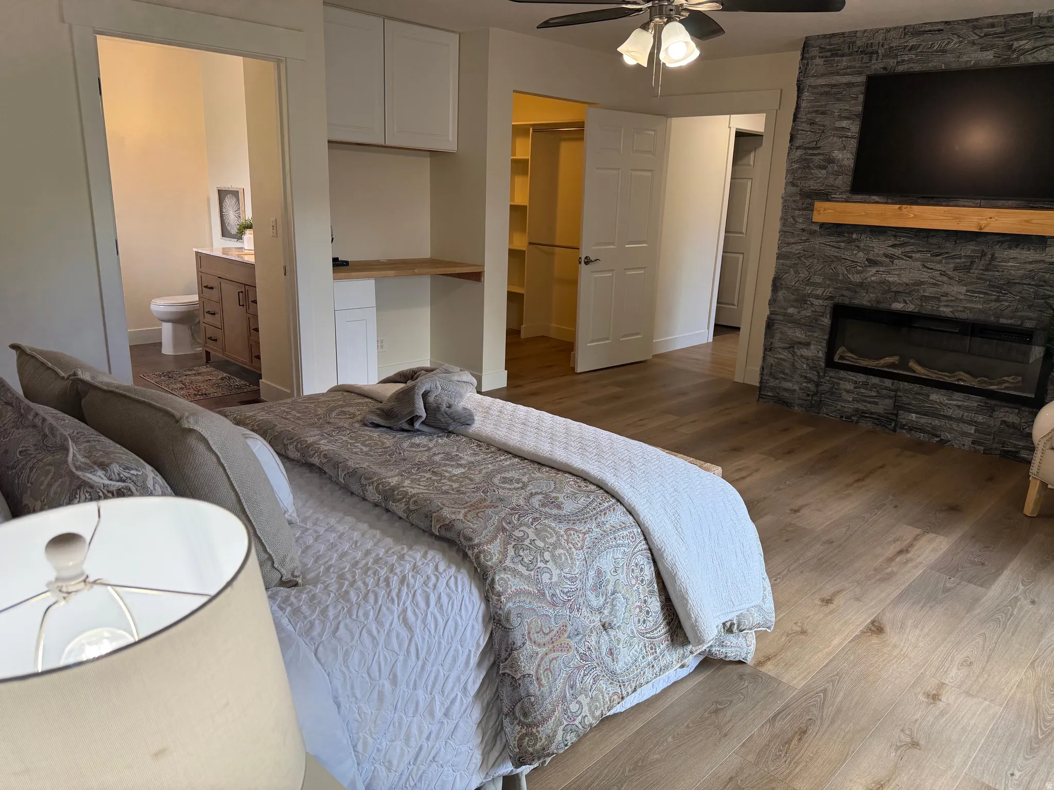 Spacious room featuring wood-finish flooring, a stacked stone fireplace with a wood mantle, and a ceiling fan