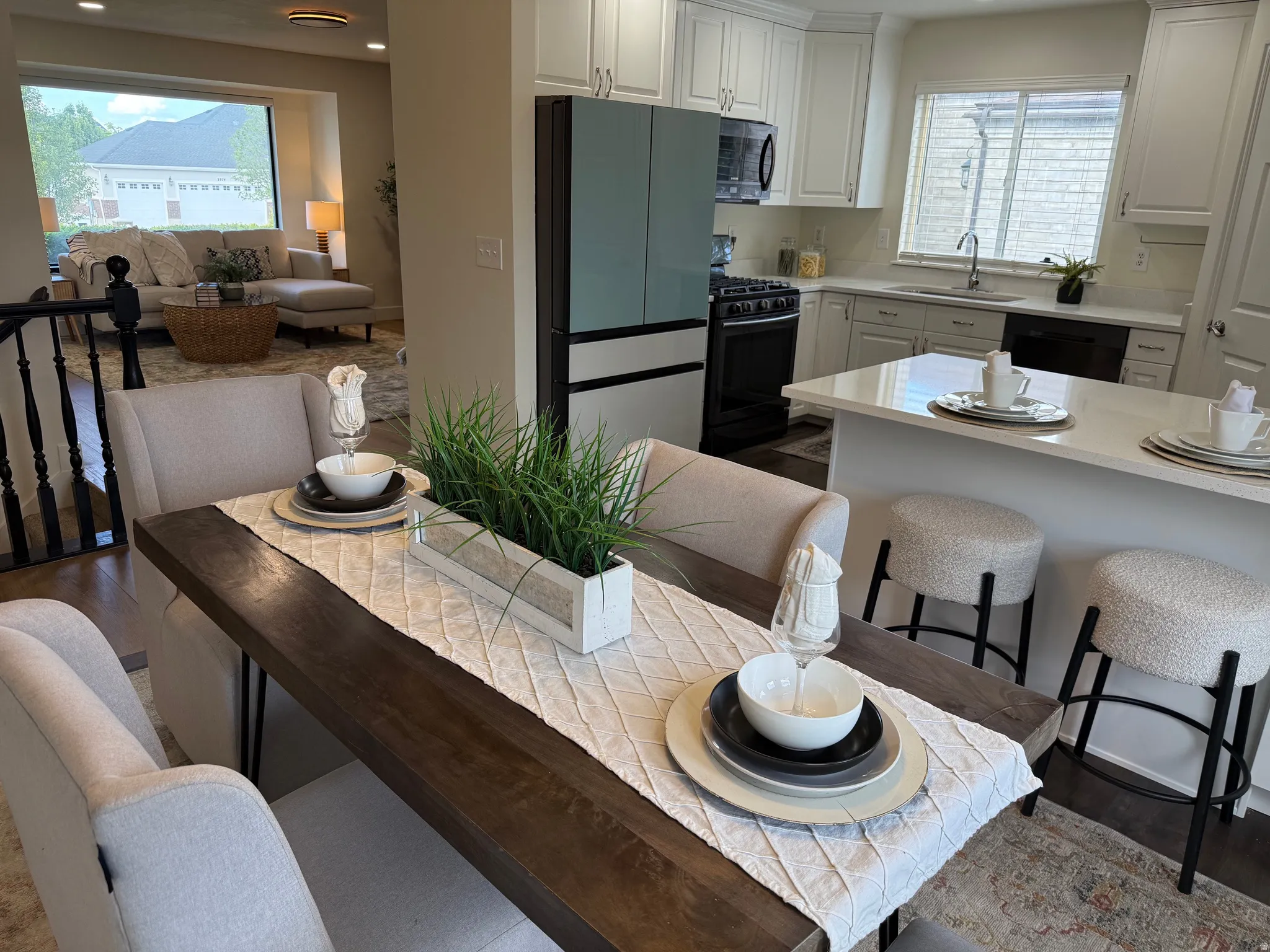 Open-concept kitchen and dining area featuring a light wood-finish dining table, white shaker cabinetry, light-toned countertops, and stainless steel appliances