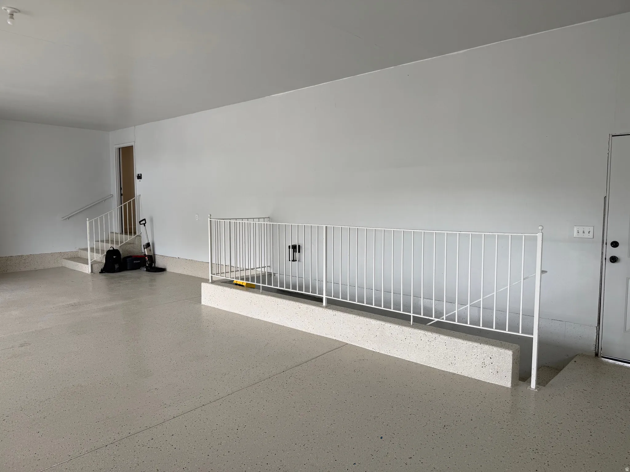 Spacious garage featuring a light-colored epoxy floor coating, white painted walls, and a white metal staircase railing with wide stair access to basement.