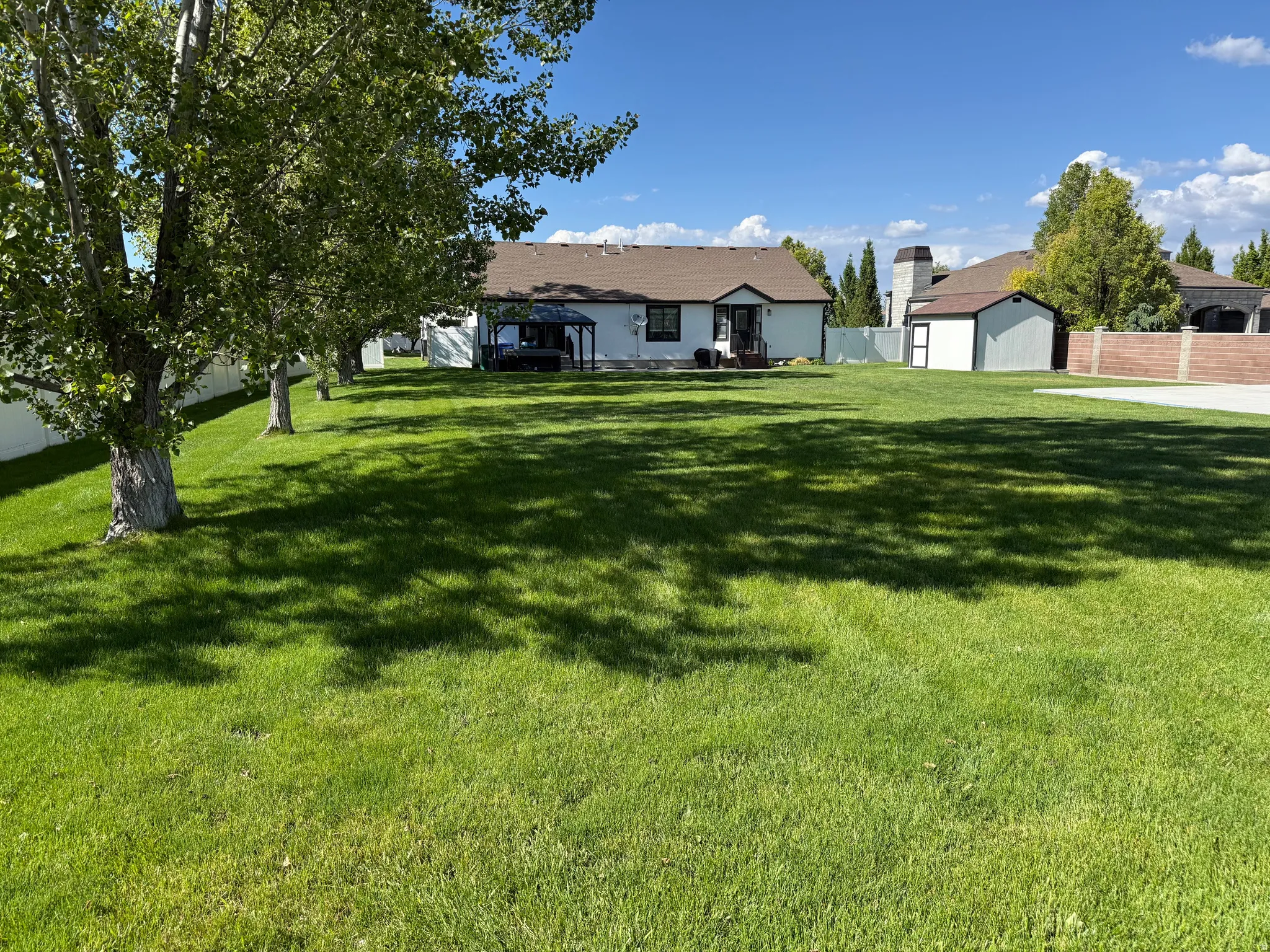 Expansive green lawn with mature trees and a white privacy fence