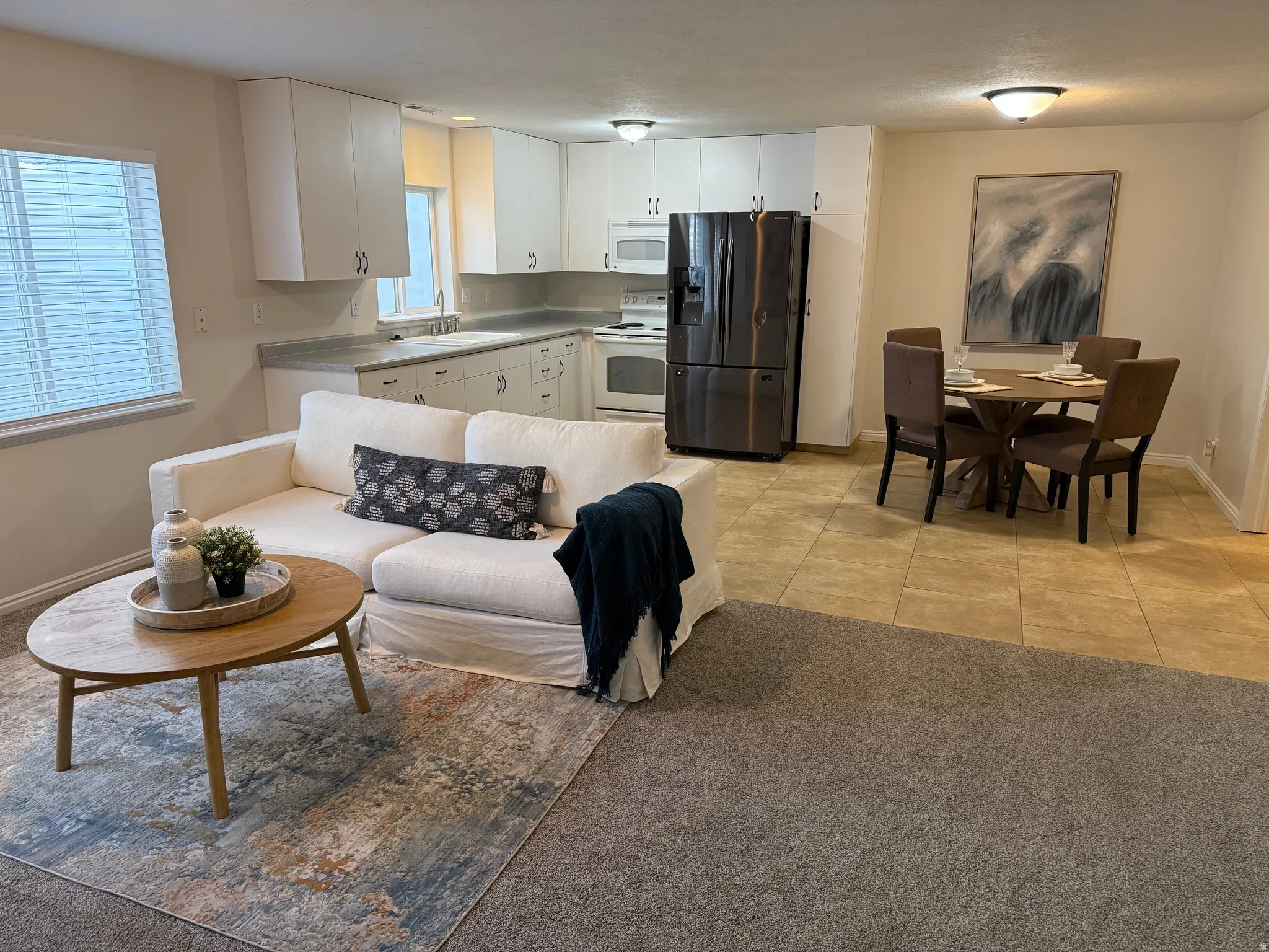 Open-concept living space featuring a kitchen with white cabinetry and stainless steel appliances, a dining area with tile flooring, and a carpeted living area