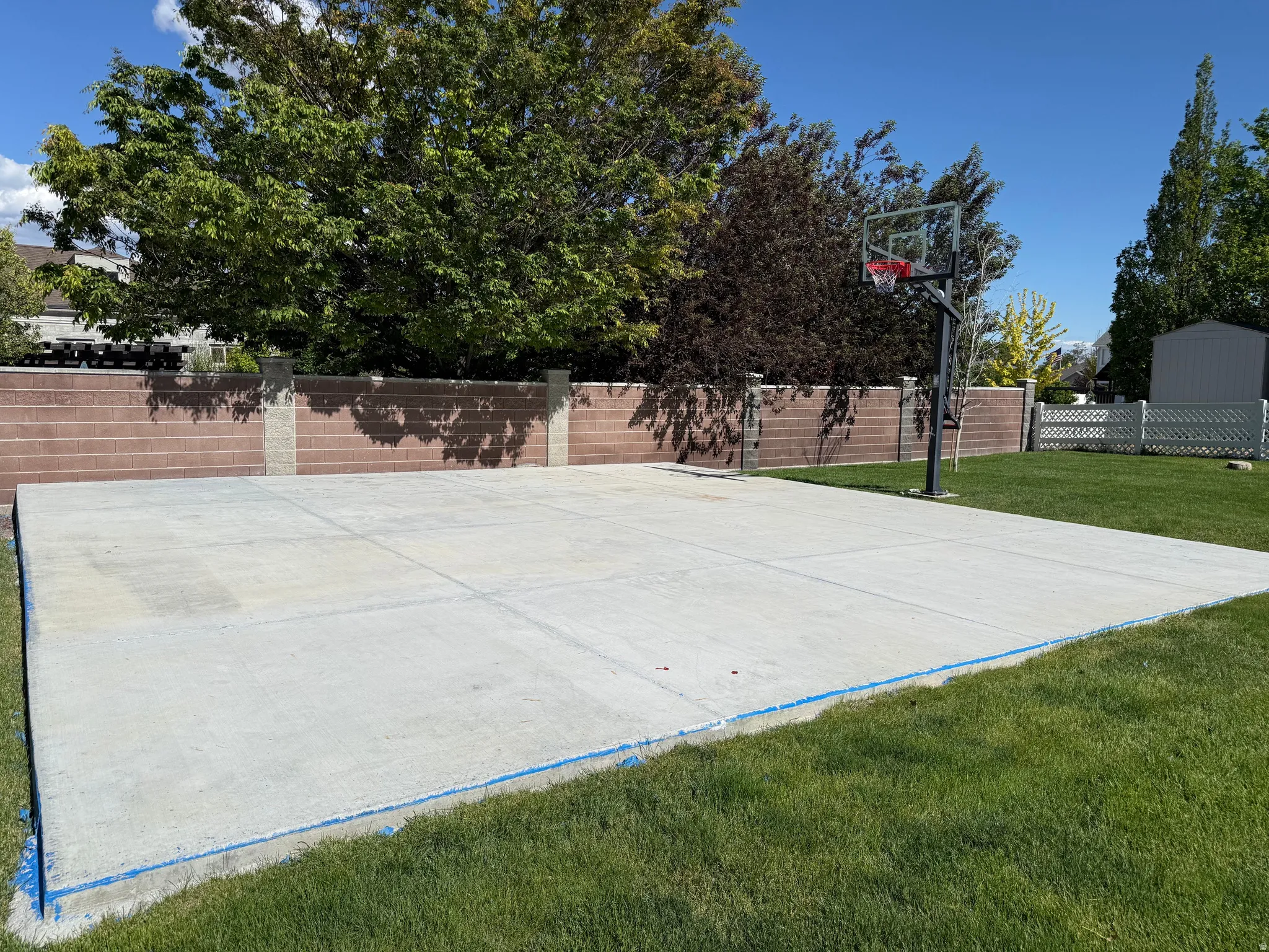 Expansive concrete pad and basketball hoop framed by a block privacy wall and manicured lawn
